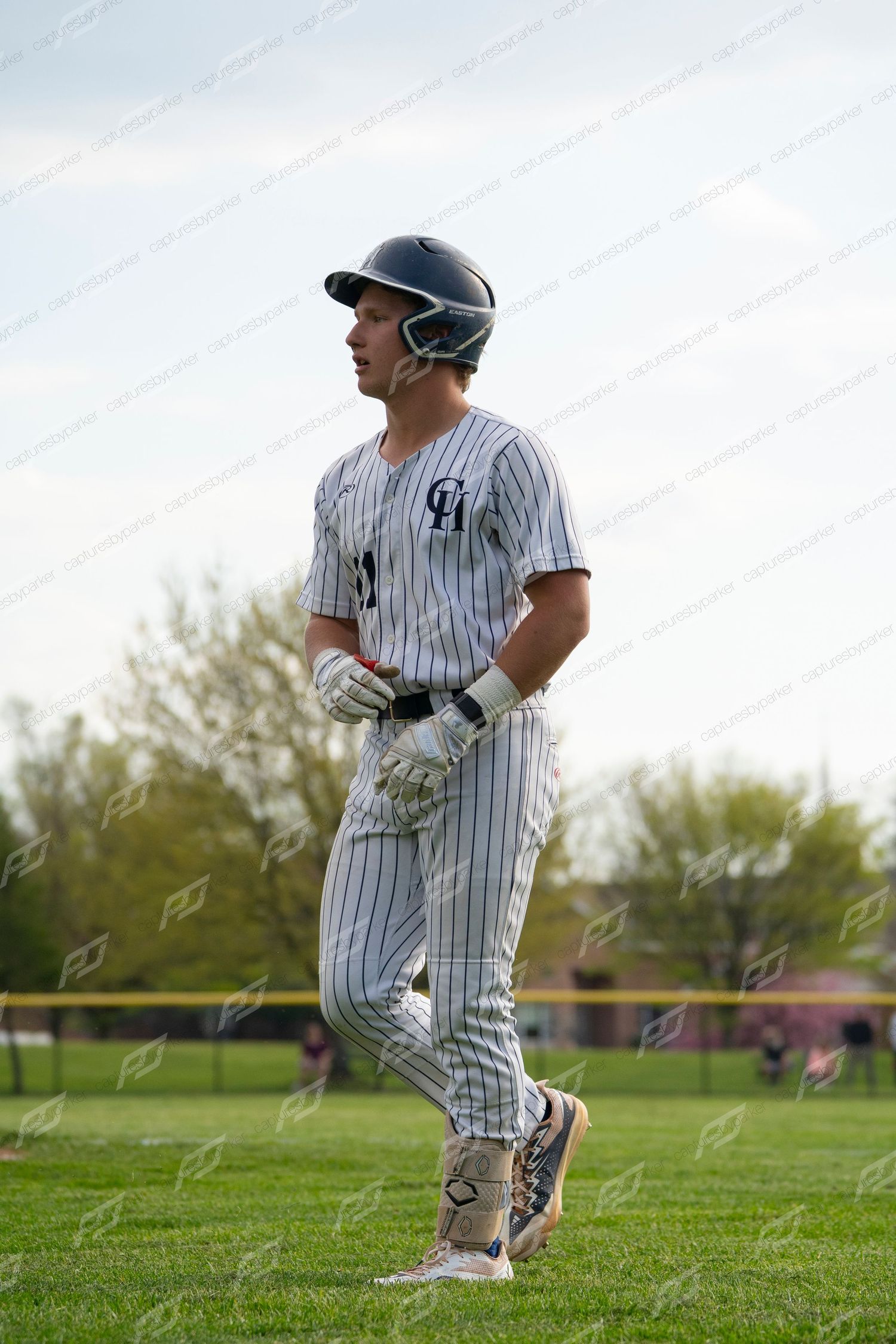 Baseball player in white pinstripe uniform and navy helmet stands on field during a game.