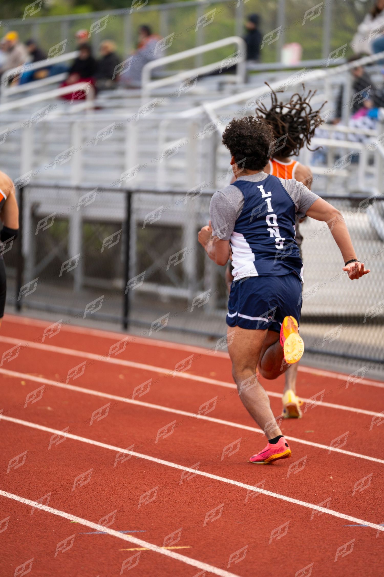Male sprinter with dreadlocks runs in navy uniform on red track during competition.