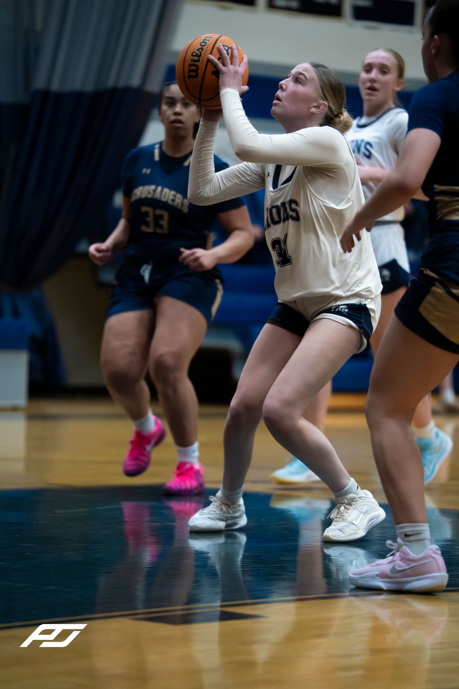 Female Lions basketball player drives to the basket for a layup against Crusaders defenders during a high school game.