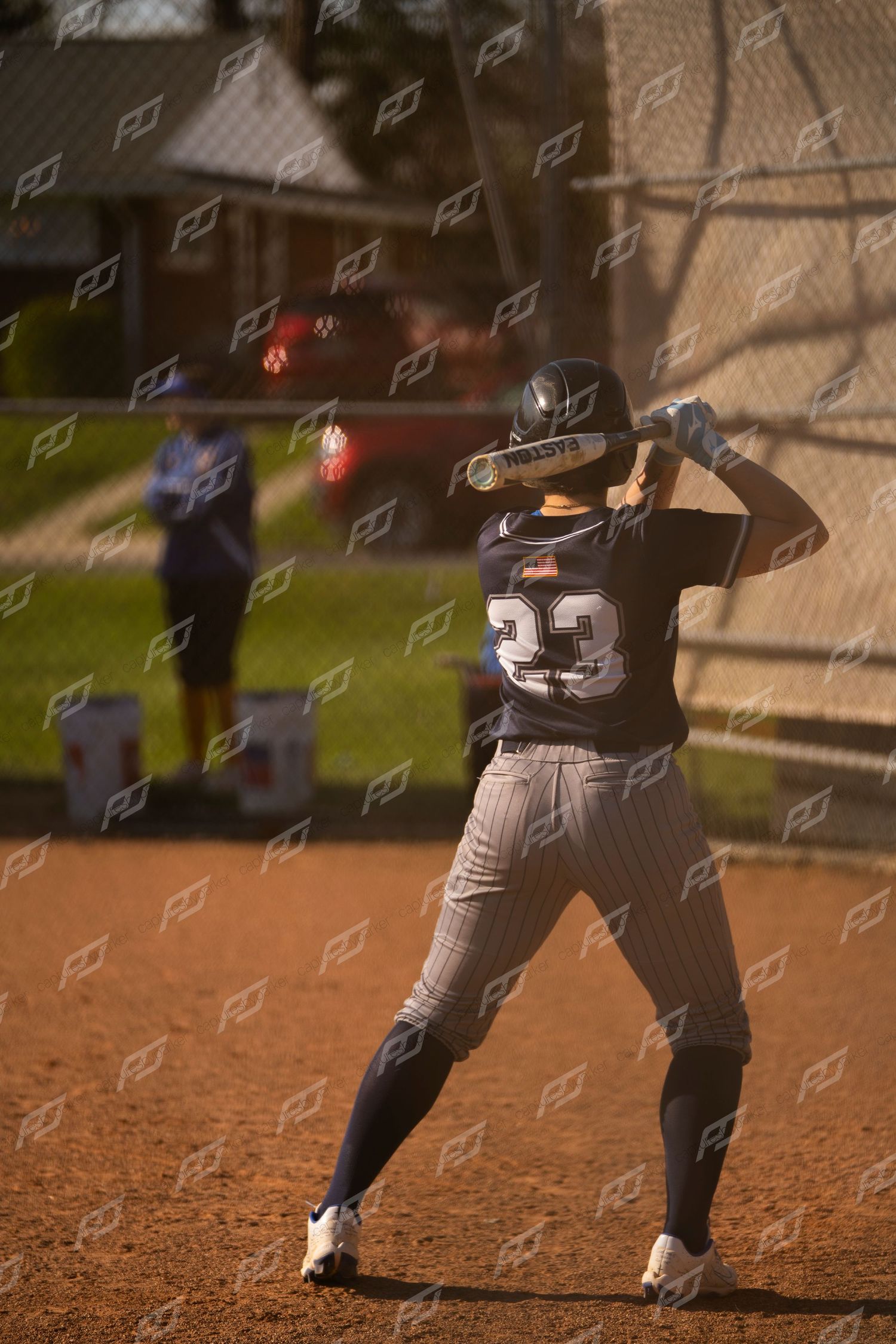 Softball player number 23 in navy uniform stands ready to bat at home plate.