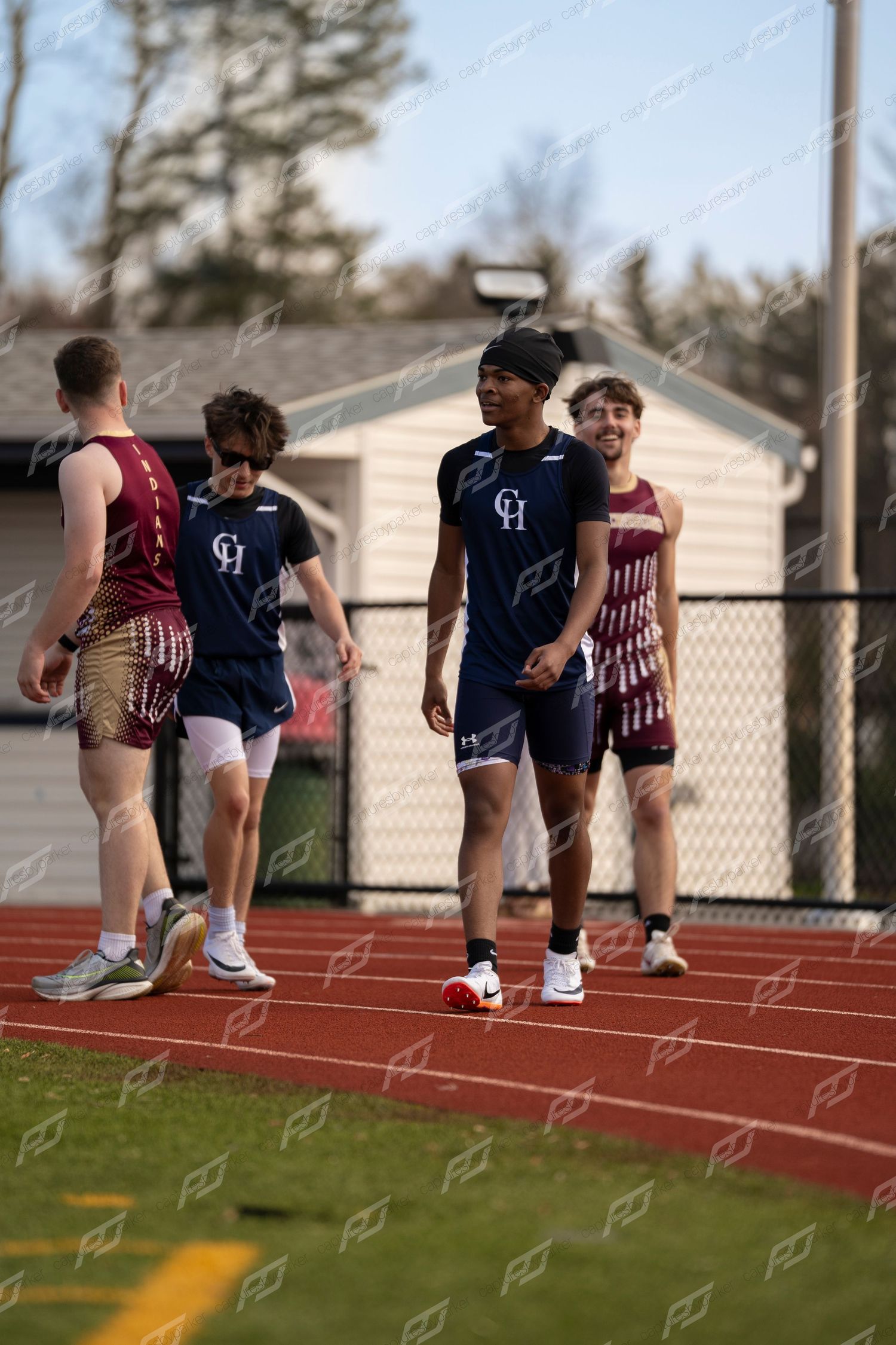High school track athletes in navy CH and maroon uniforms walk on red track.