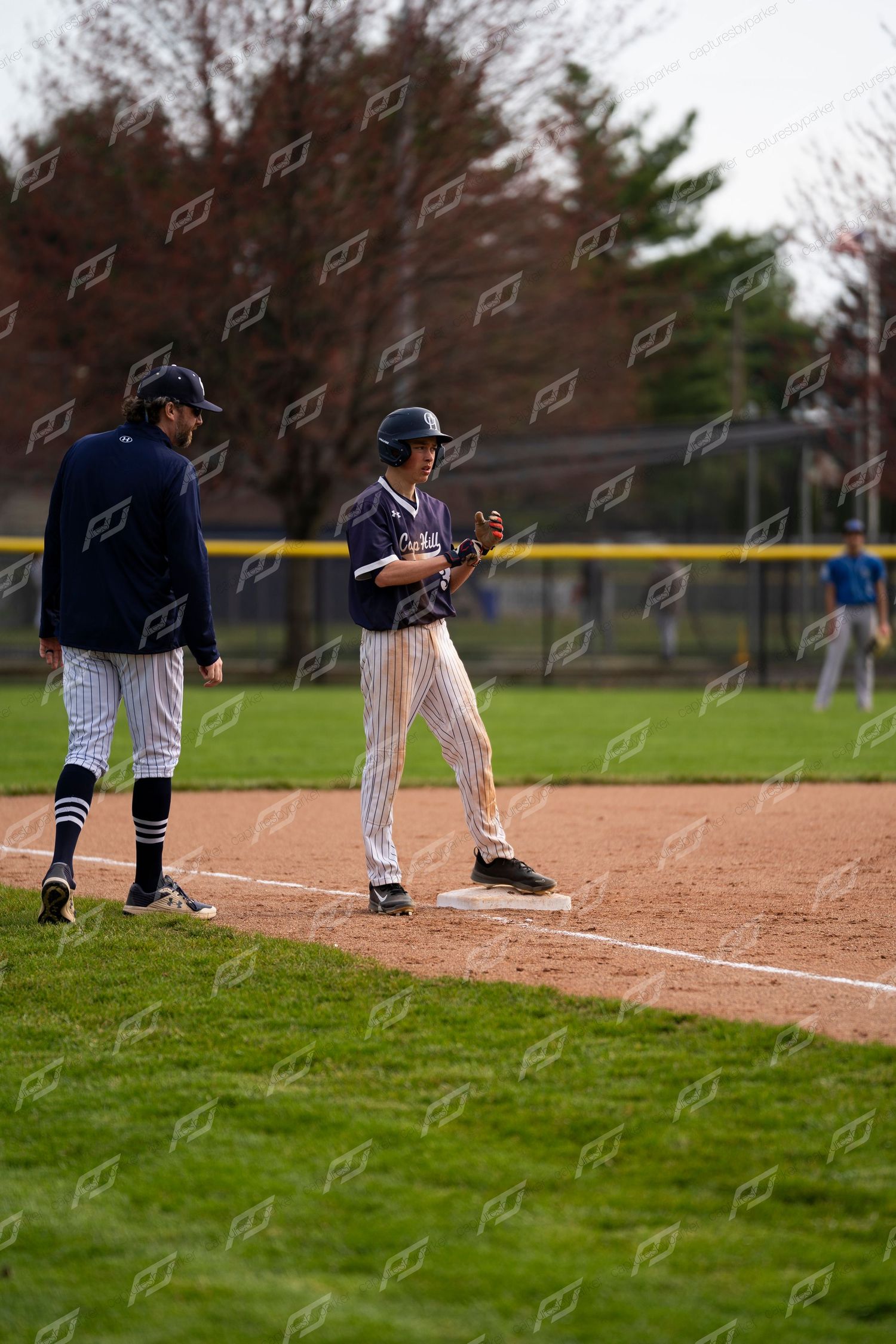 Youth baseball player stands on first base while coach provides guidance during a game.