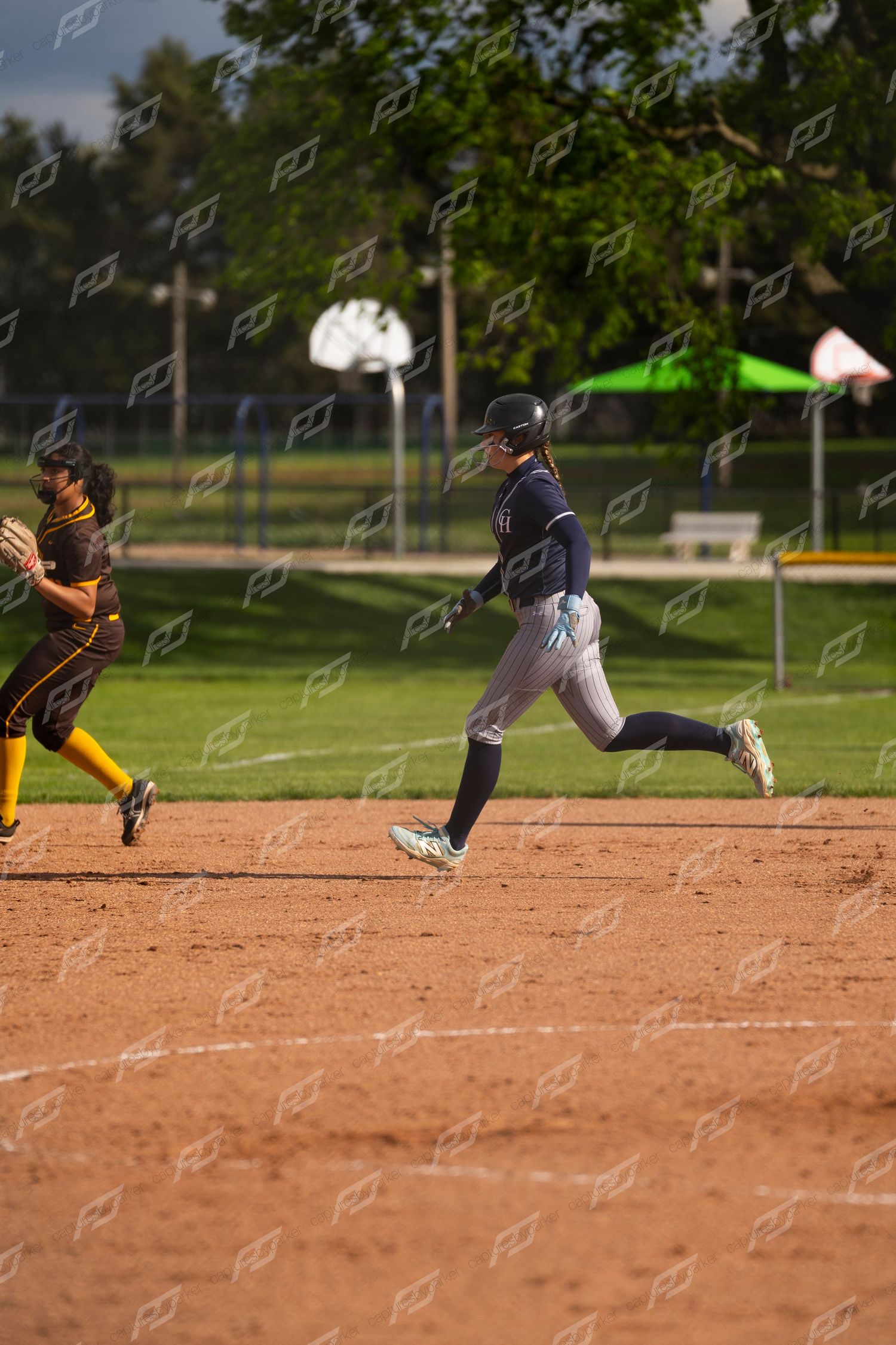 Female softball player in navy uniform sprints past an opposing player during a softball game.