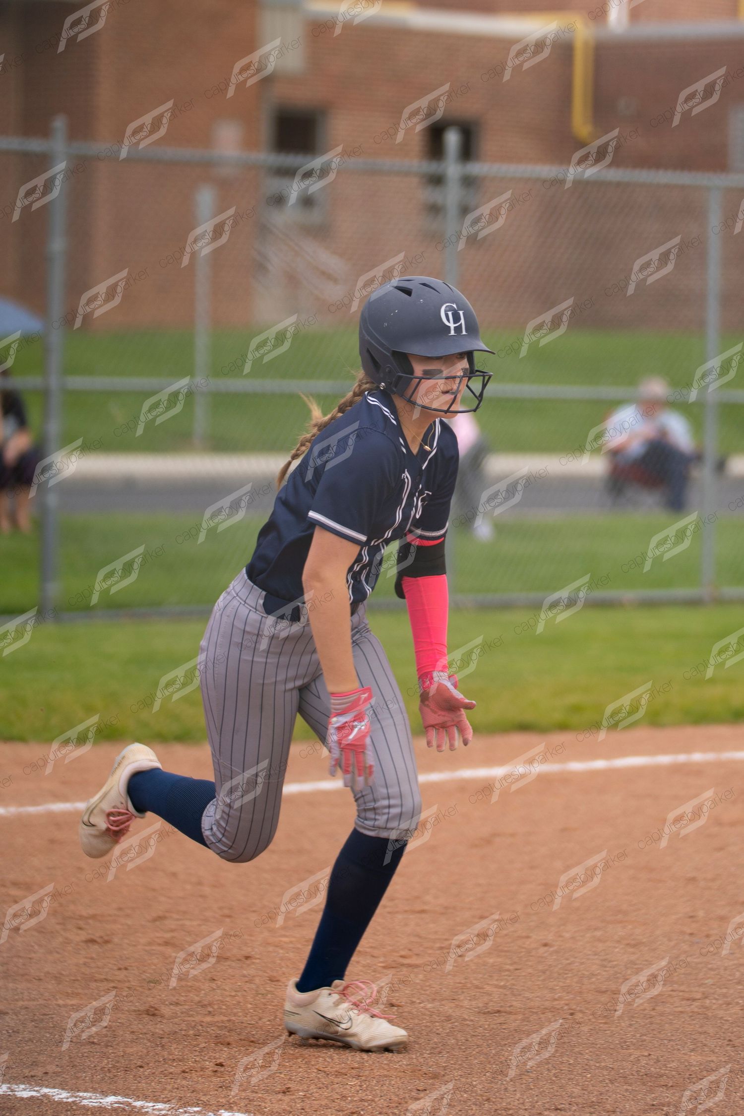 Female softball player in navy pinstripe uniform runs the bases during a game.