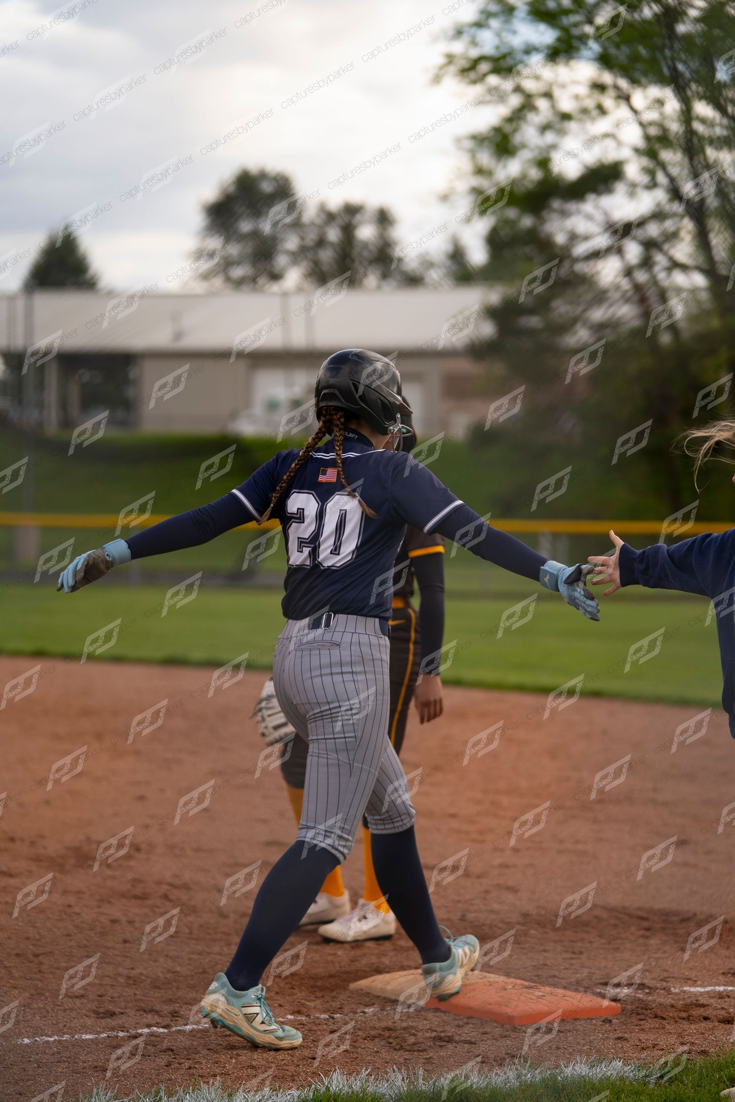 Female softball player number 20 in navy uniform reaches first base during outdoor game.