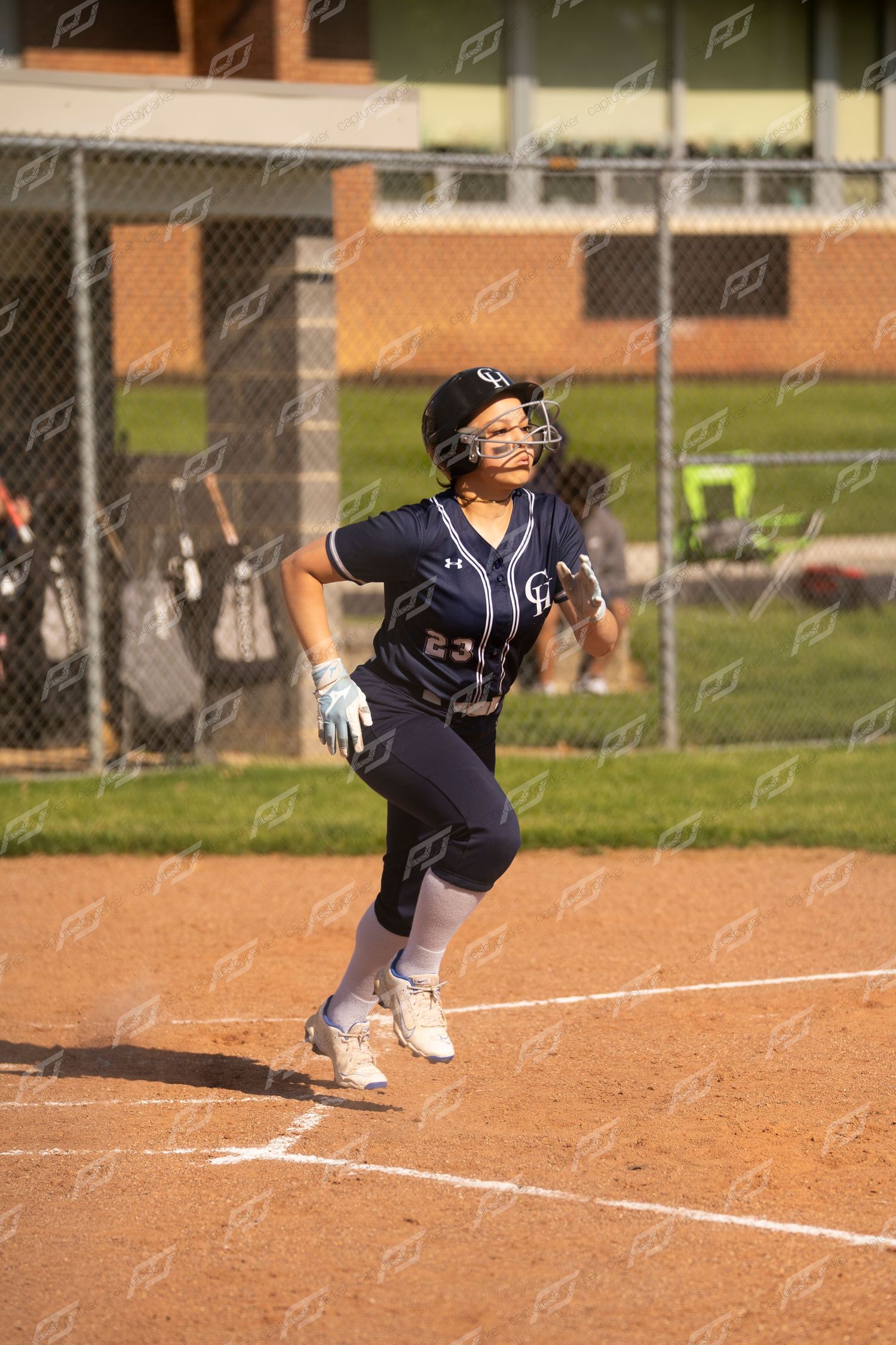 Female softball player number 23 in navy uniform runs toward first base after hit.