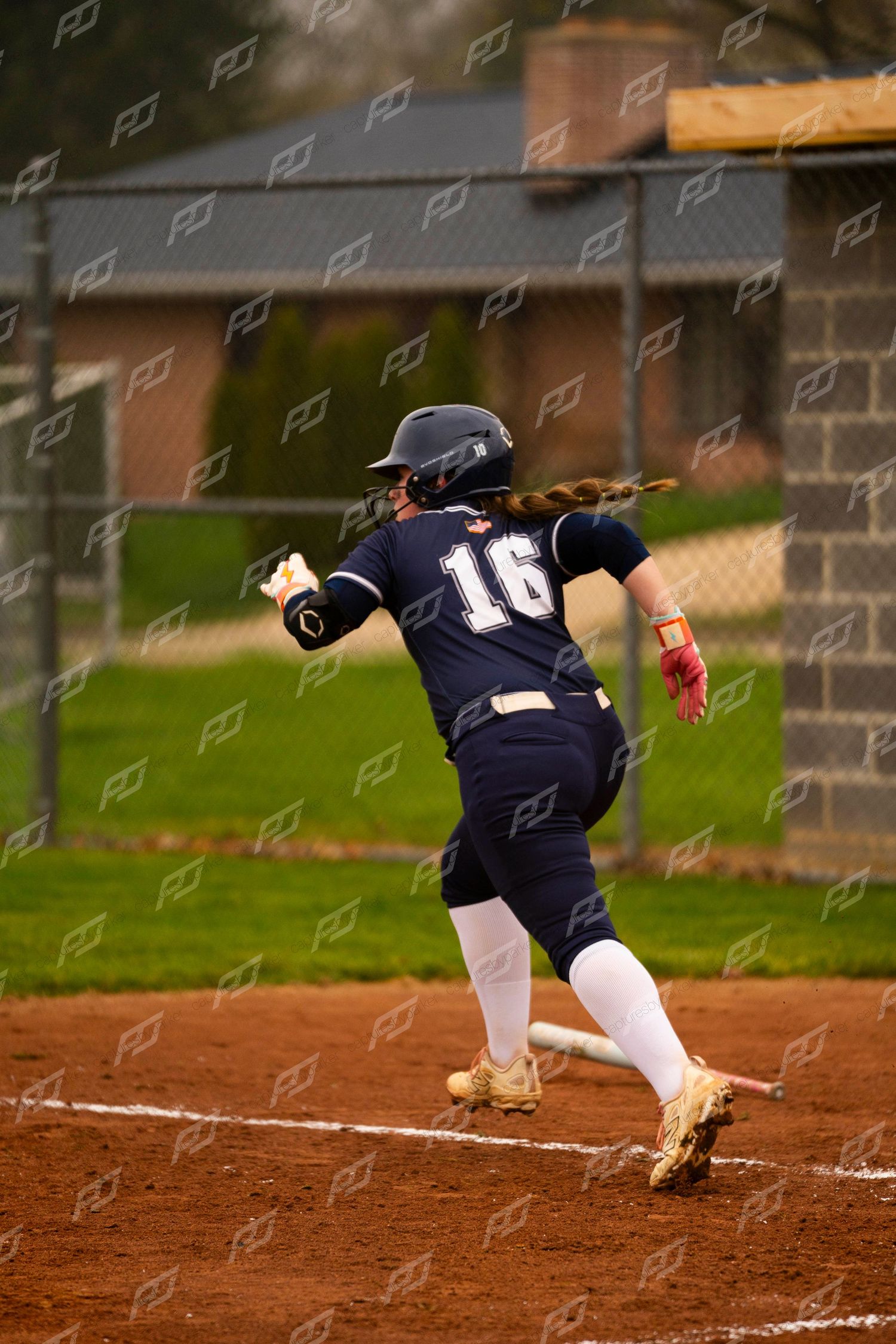 Softball player number 16 in navy uniform sprints down the baseline during game.