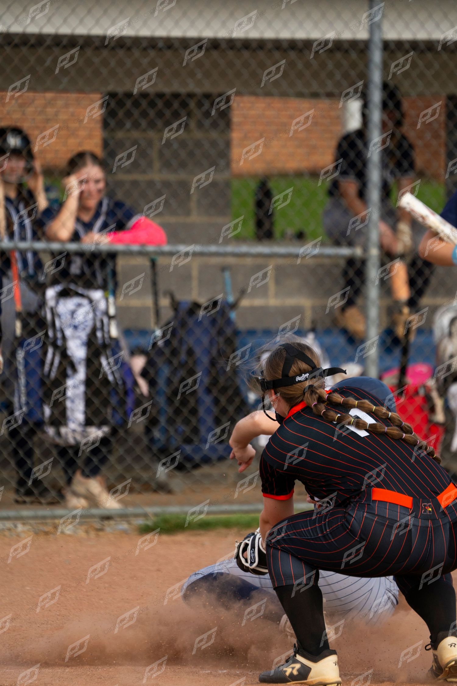 Softball fielder in black uniform tags out sliding runner in a cloud of dust during competitive game.