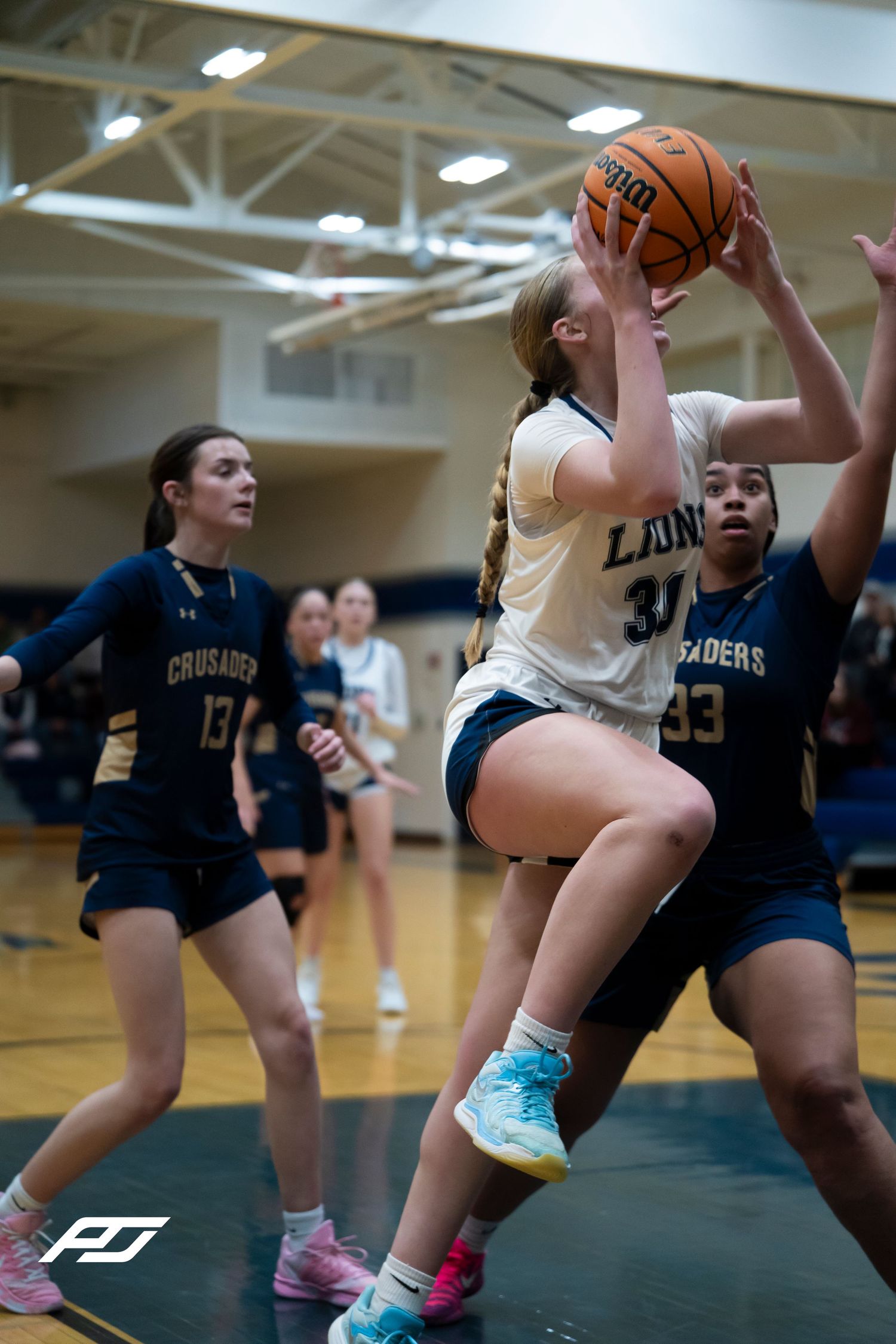 Lions #34 female player drives to basket between two Crusaders defenders during high school basketball game.