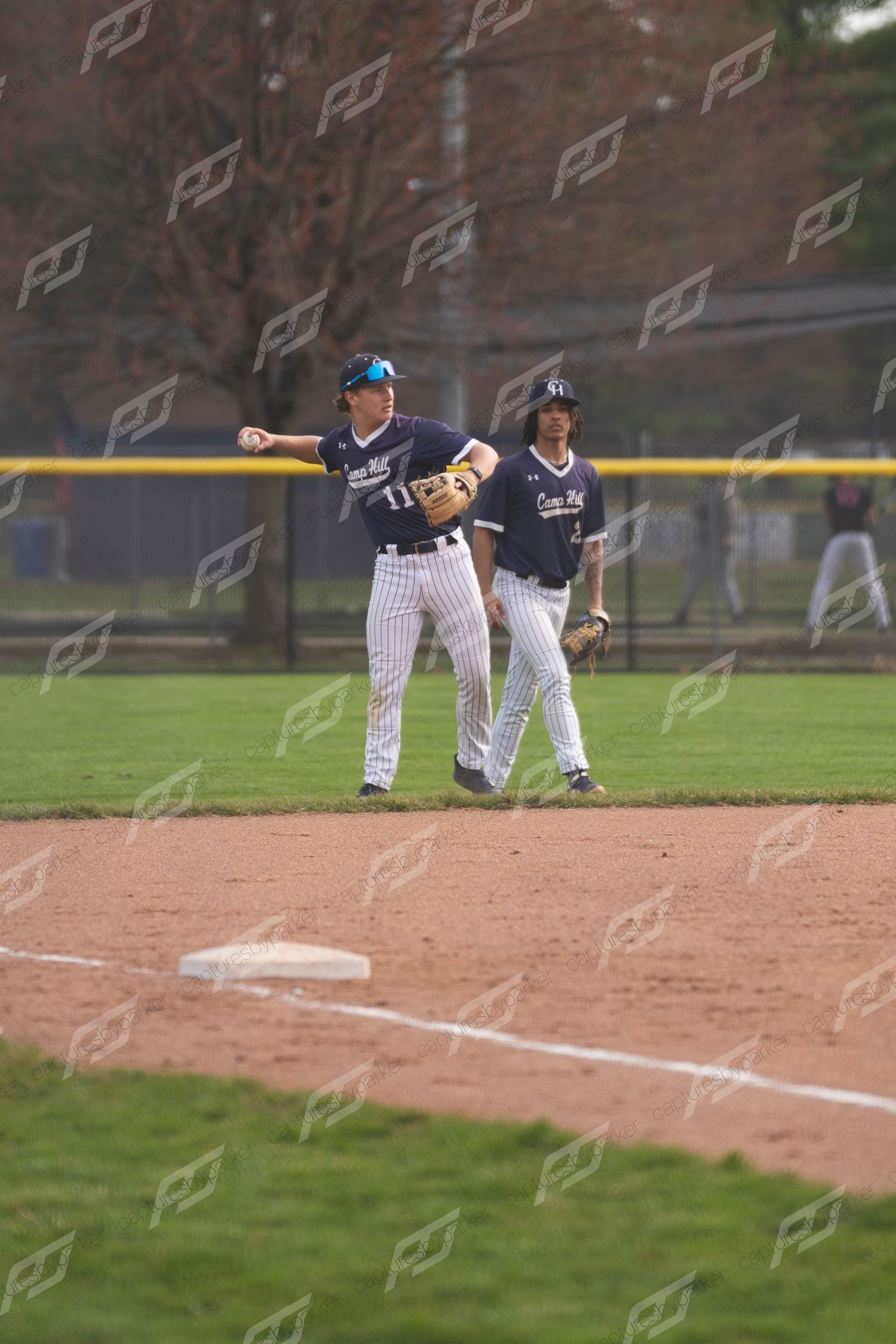 High school baseball infielder in navy pinstripe uniform throwing to first base during a spring game.