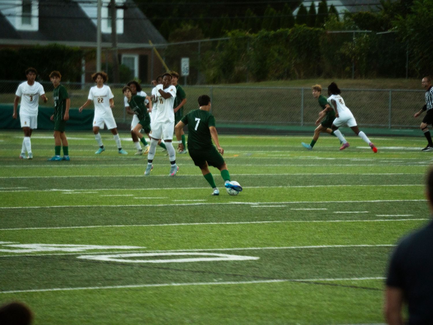 Trinity soccer player #7 dribbles ball on turf field during competitive match against white-uniformed opponents.