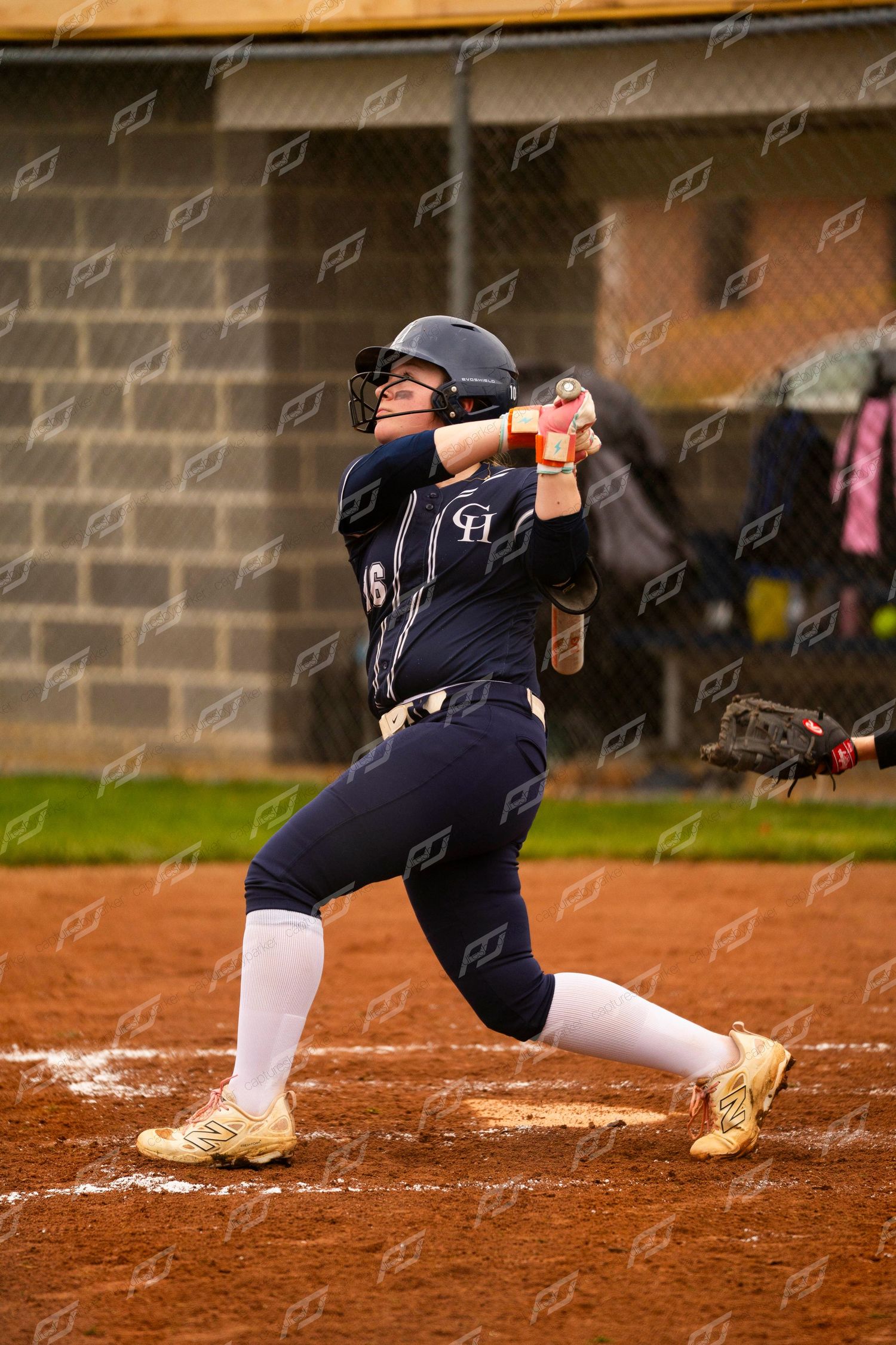 Female softball player #16 in navy uniform follows through on powerful swing during competitive game.