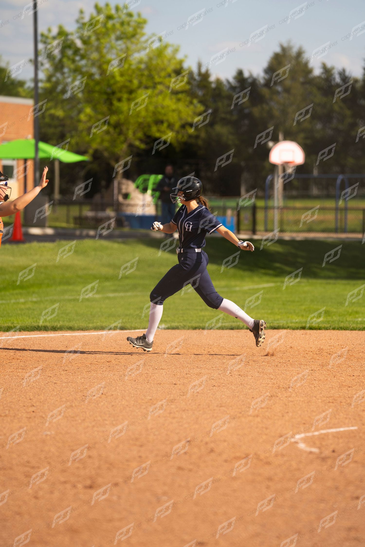 Youth softball player in navy uniform rounds second base during sunny outdoor game.