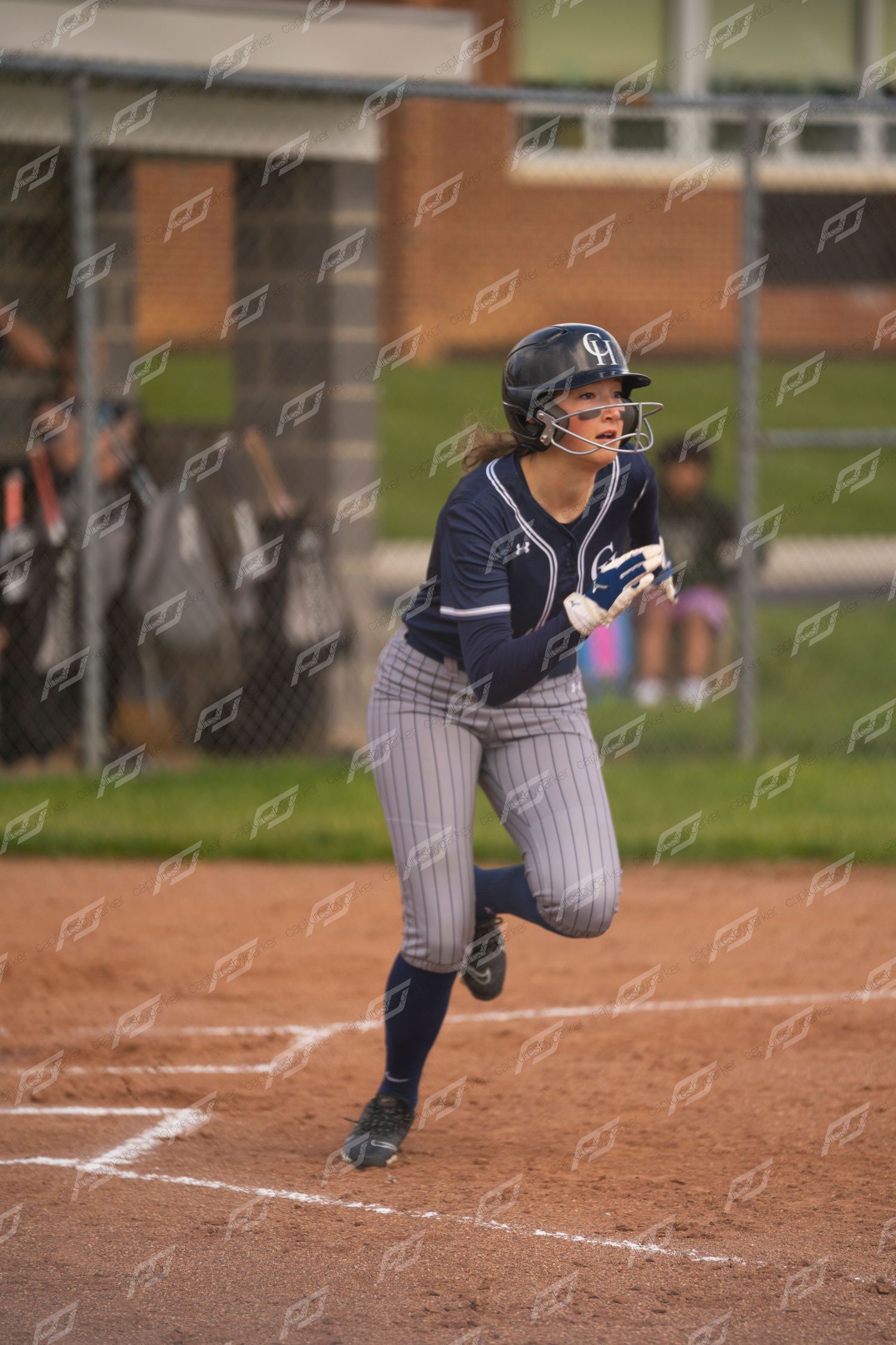 Female softball player in navy GH uniform runs bases during outdoor game.