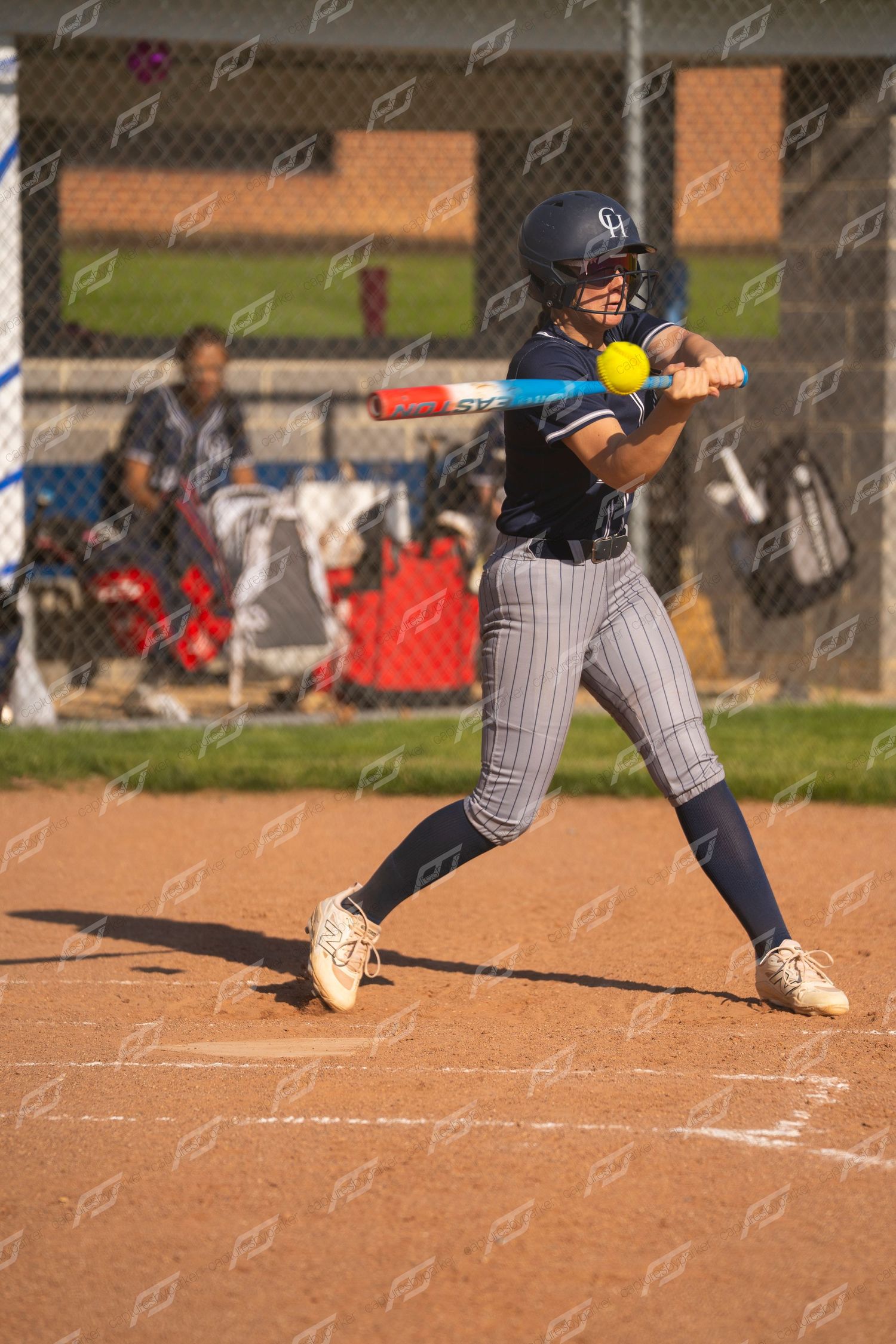 Softball player in navy uniform makes contact with yellow ball using blue bat during game.