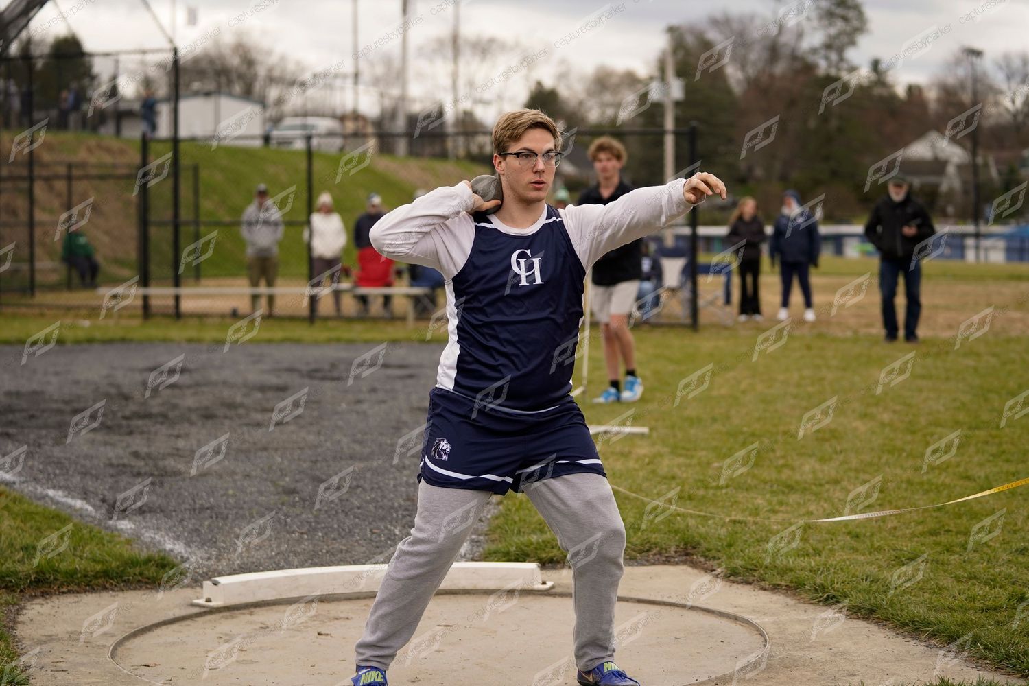 Young male athlete in navy uniform winds up for a discus throw at a high school track meet.