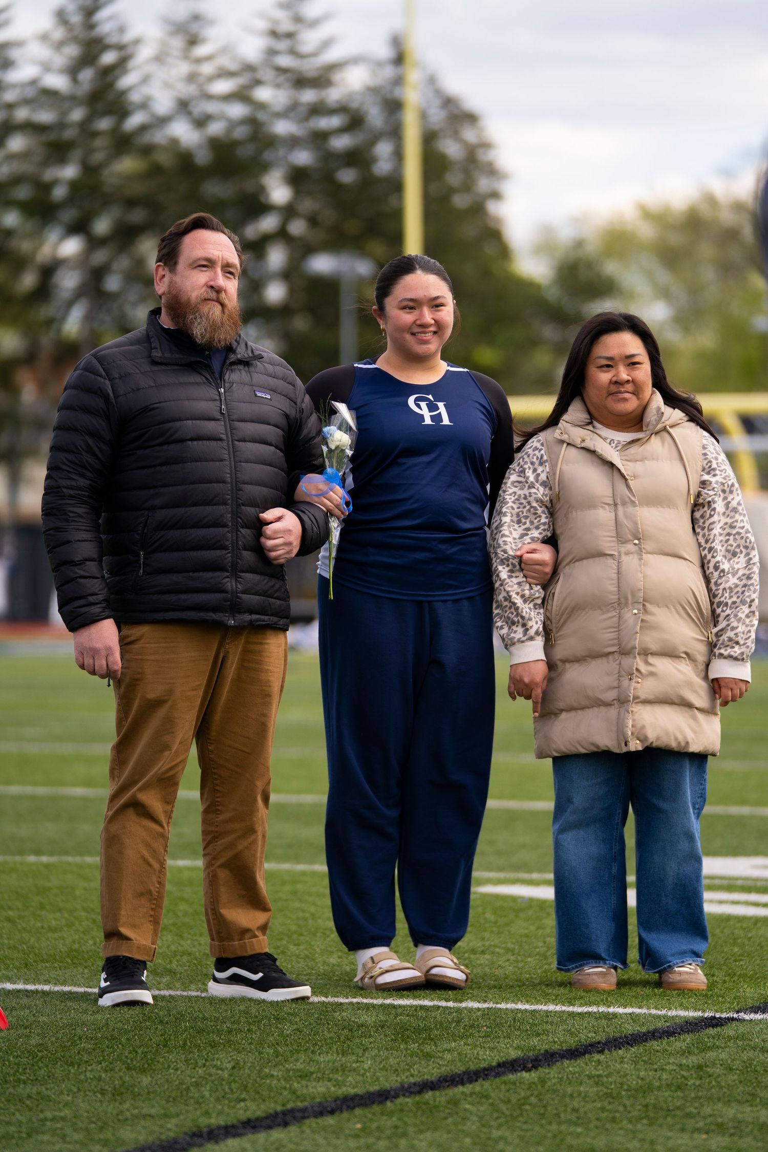Three people posing together on a football field during a school sports senior day ceremony.
