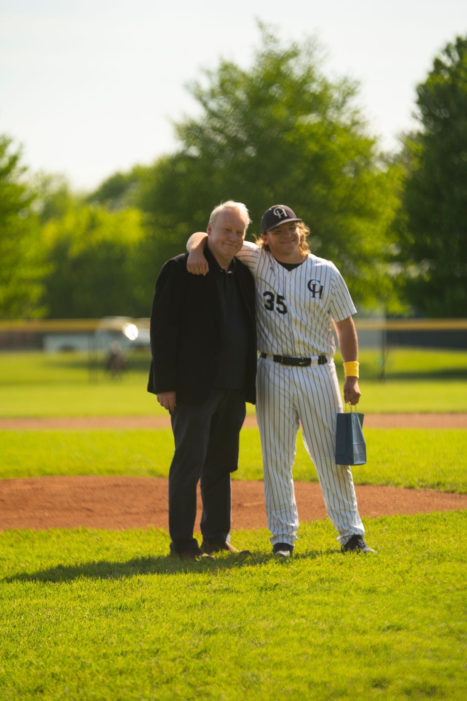 Baseball player #35 in pinstripe uniform shares a warm embrace with an elderly man on a sunny baseball field.