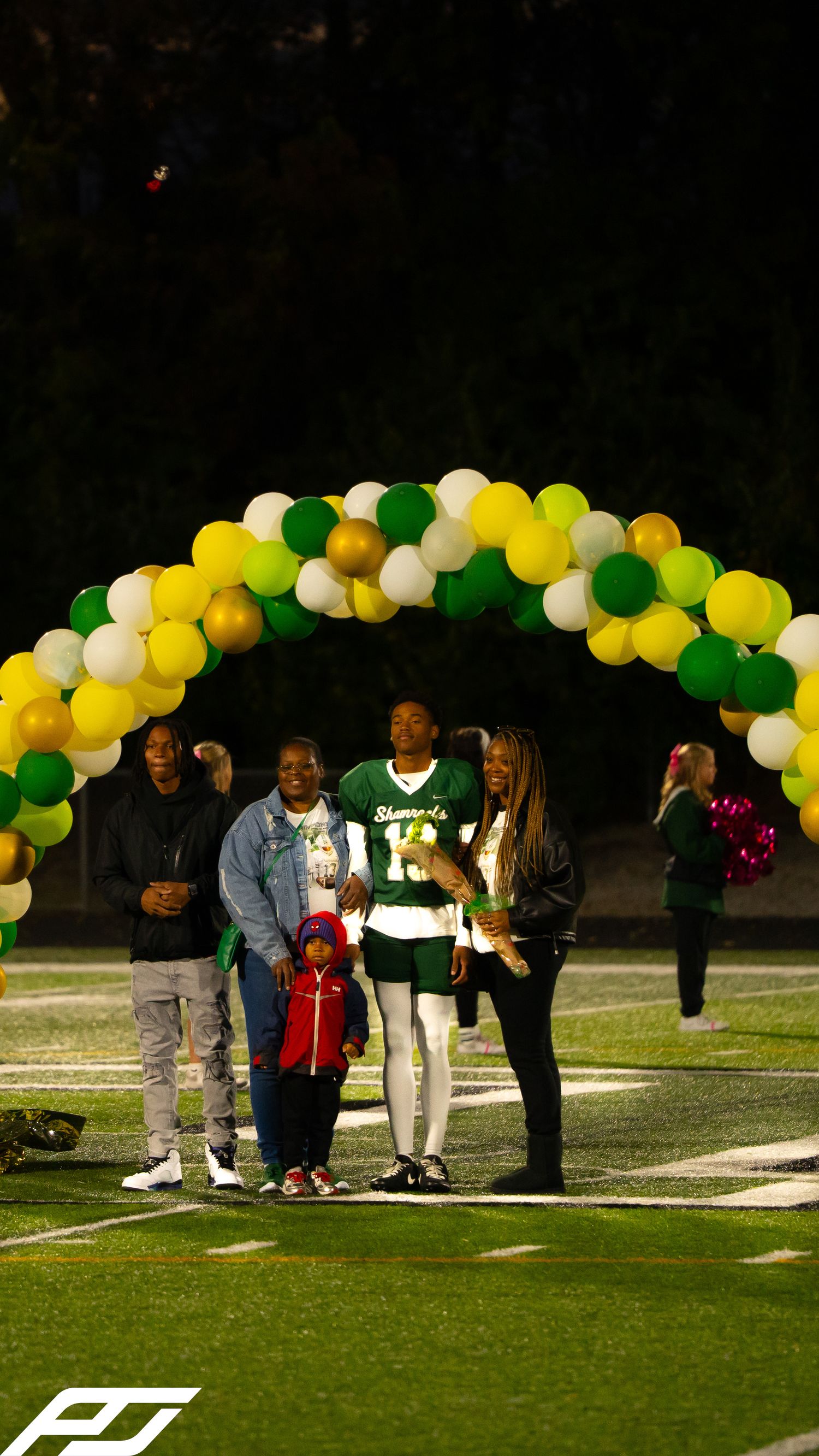Shamrocks football player number 13 stands with family including young child under colorful balloon arch.