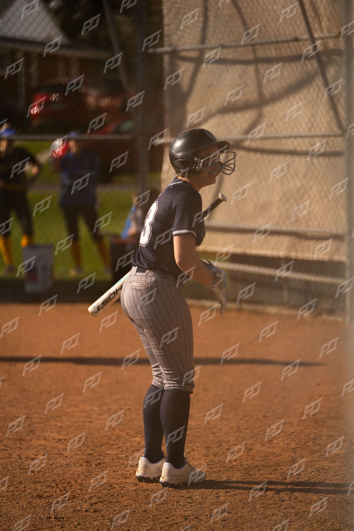 Female softball player in navy pinstripe uniform holds bat while standing on dirt field.
