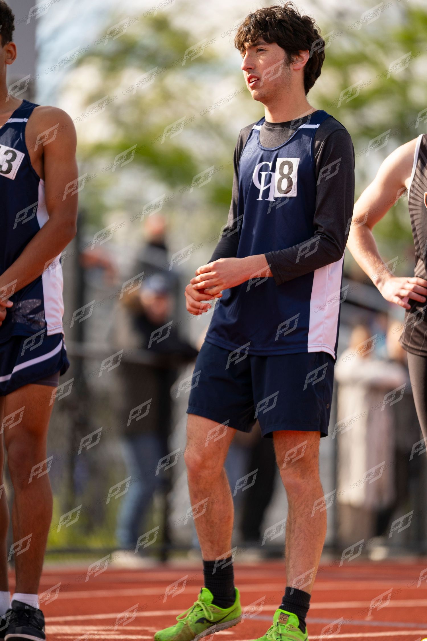 Male high school track athlete in navy GB uniform stands relaxed between race events.