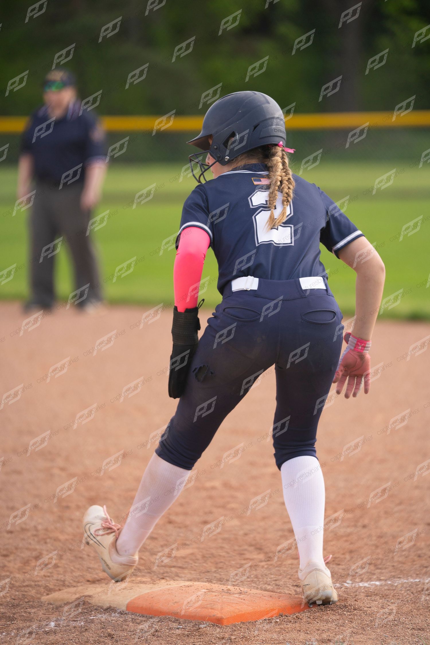 Softball player #2 in navy uniform rounds third base during a game.
