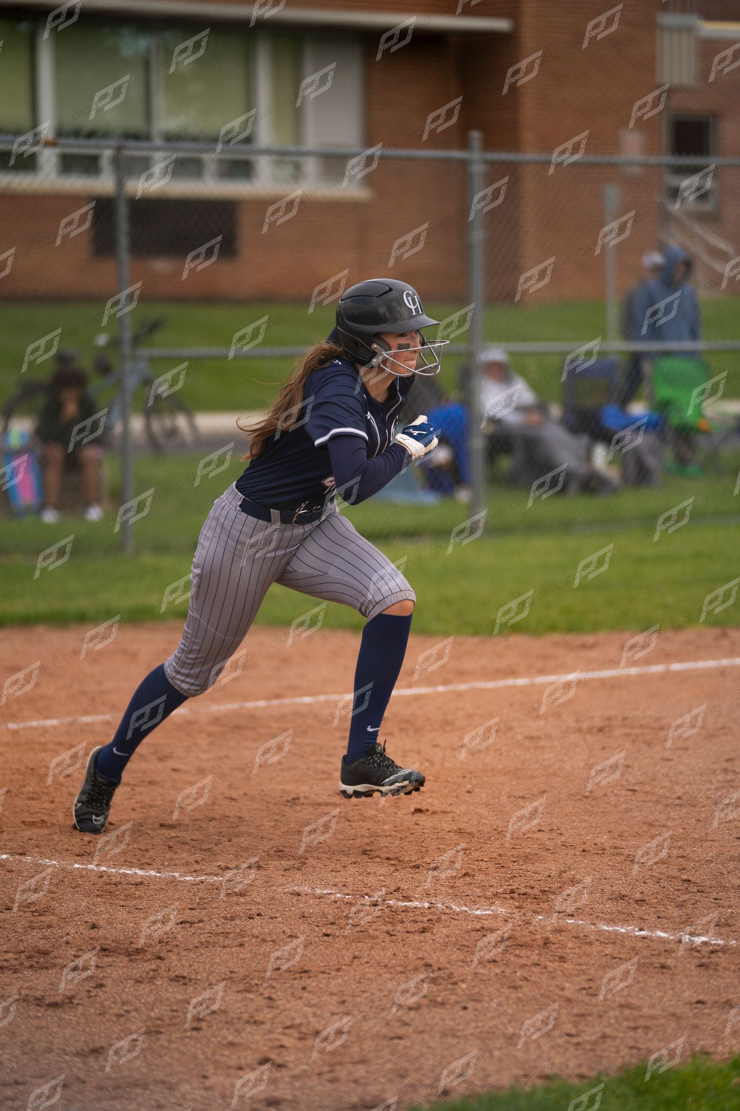 Female softball player sprints from base in navy pinstripe uniform during a game.