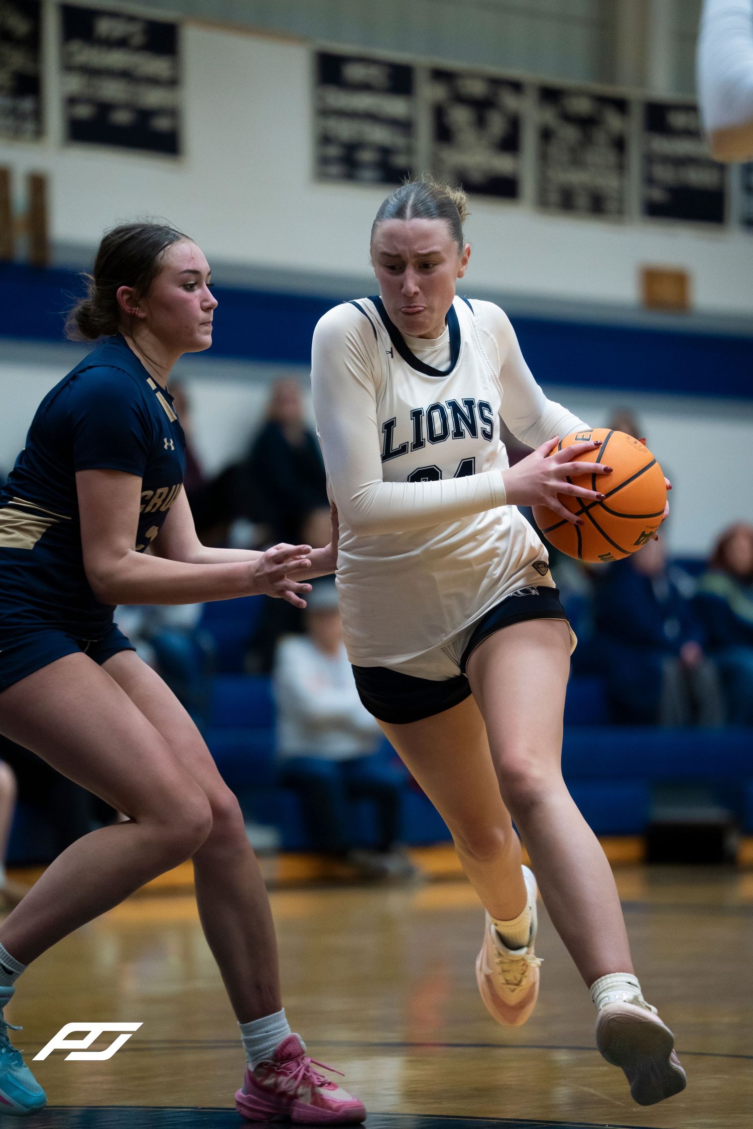 Lions #21 female basketball player drives past a defender during a competitive high school girls basketball game.