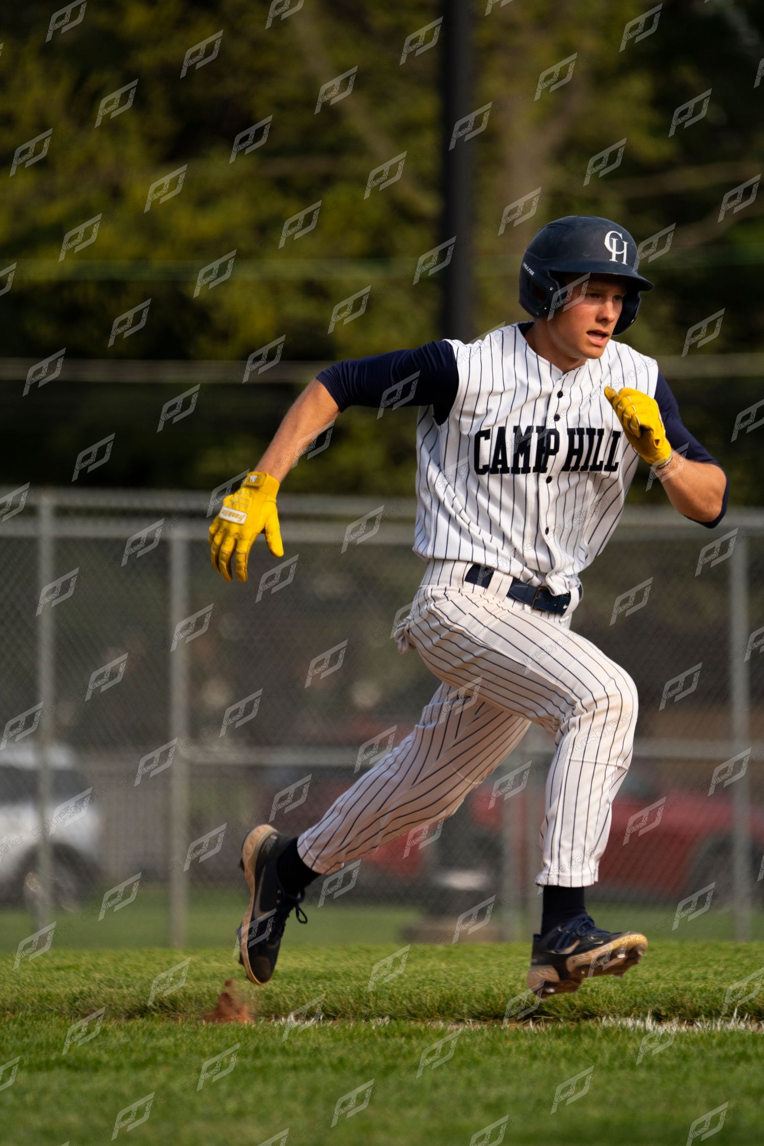 Camp Hill baseball player in pinstripe uniform sprinting the bases wearing a black helmet and yellow batting gloves.
