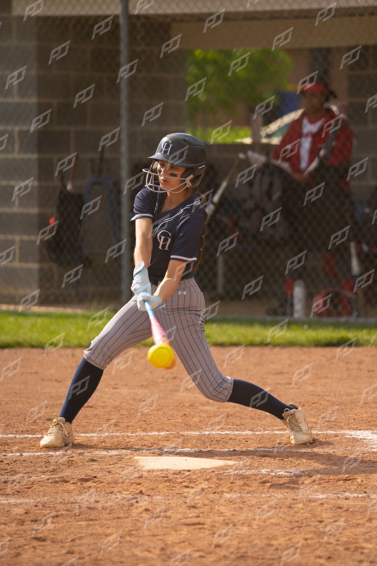 Softball batter in navy pinstripe uniform makes contact with yellow ball during a game.