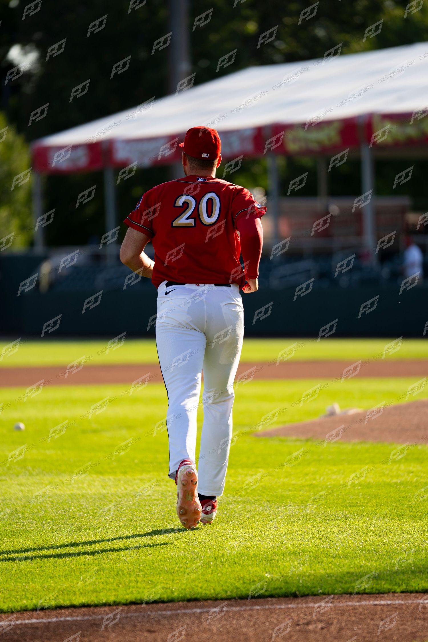 Baseball player wearing number 20 in red and white uniform jogs across the outfield grass.