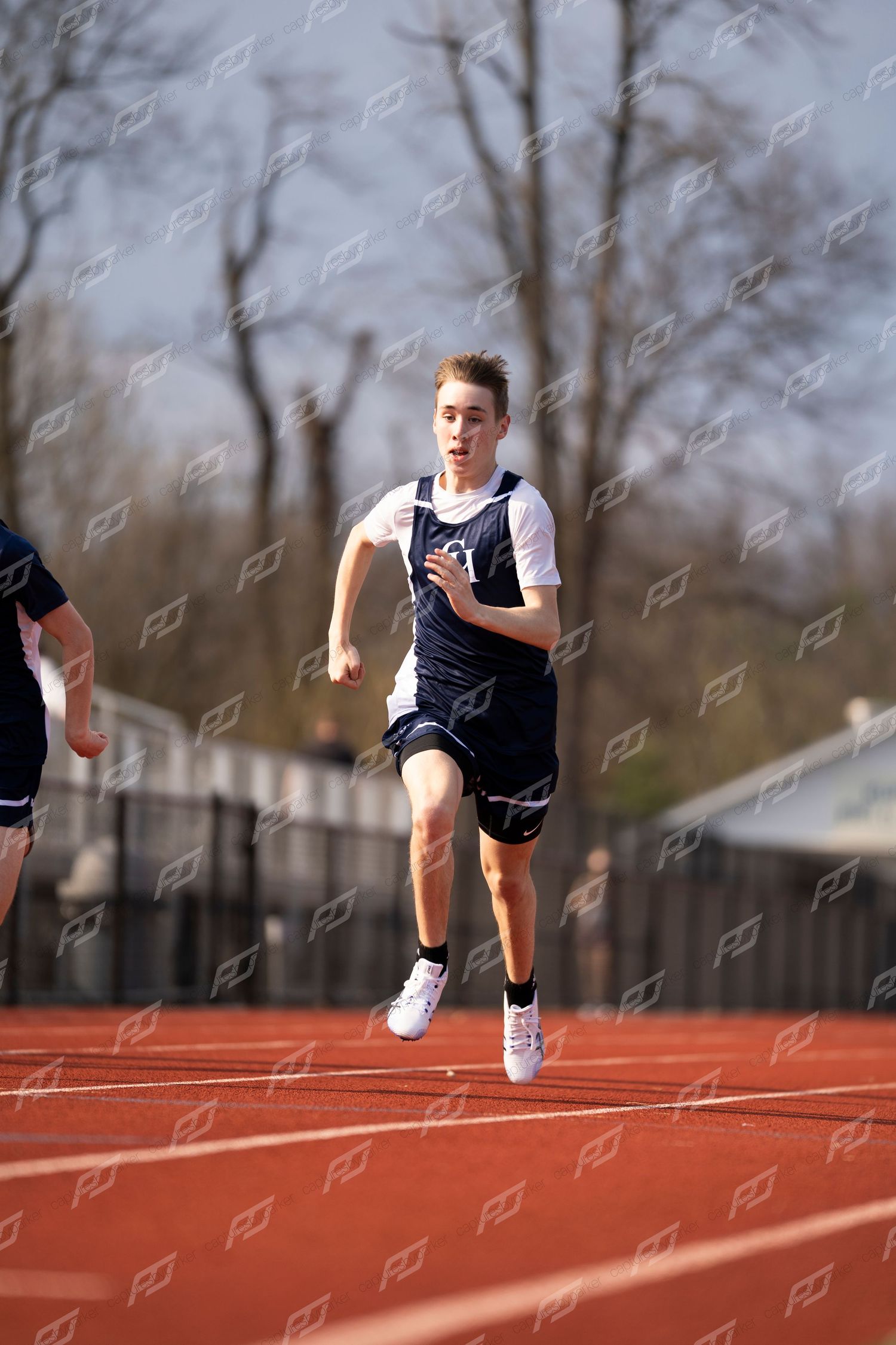Young male sprinter in navy CH uniform runs race on red outdoor track.