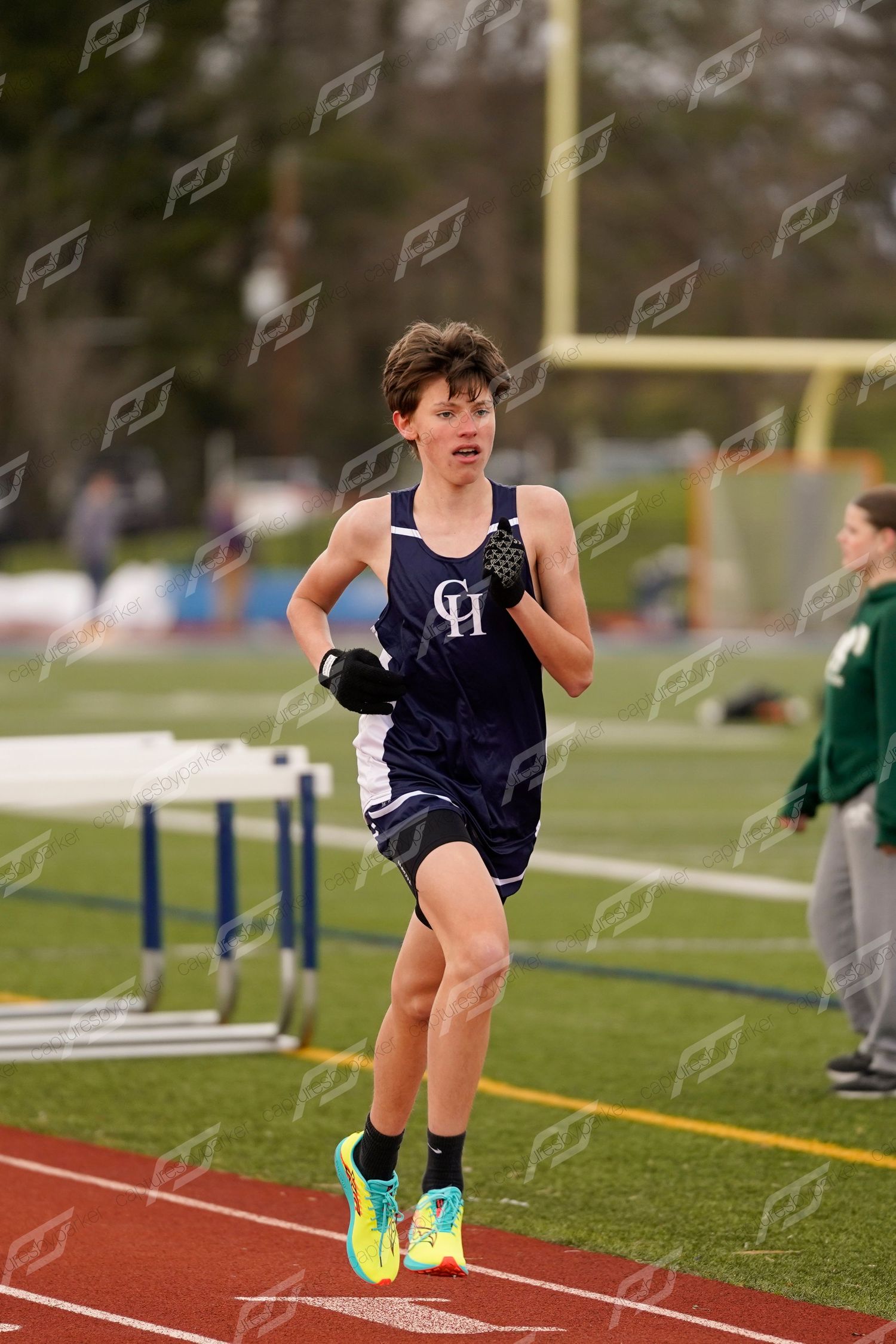 Young male runner in navy uniform sprinting on a red track wearing bright yellow shoes.