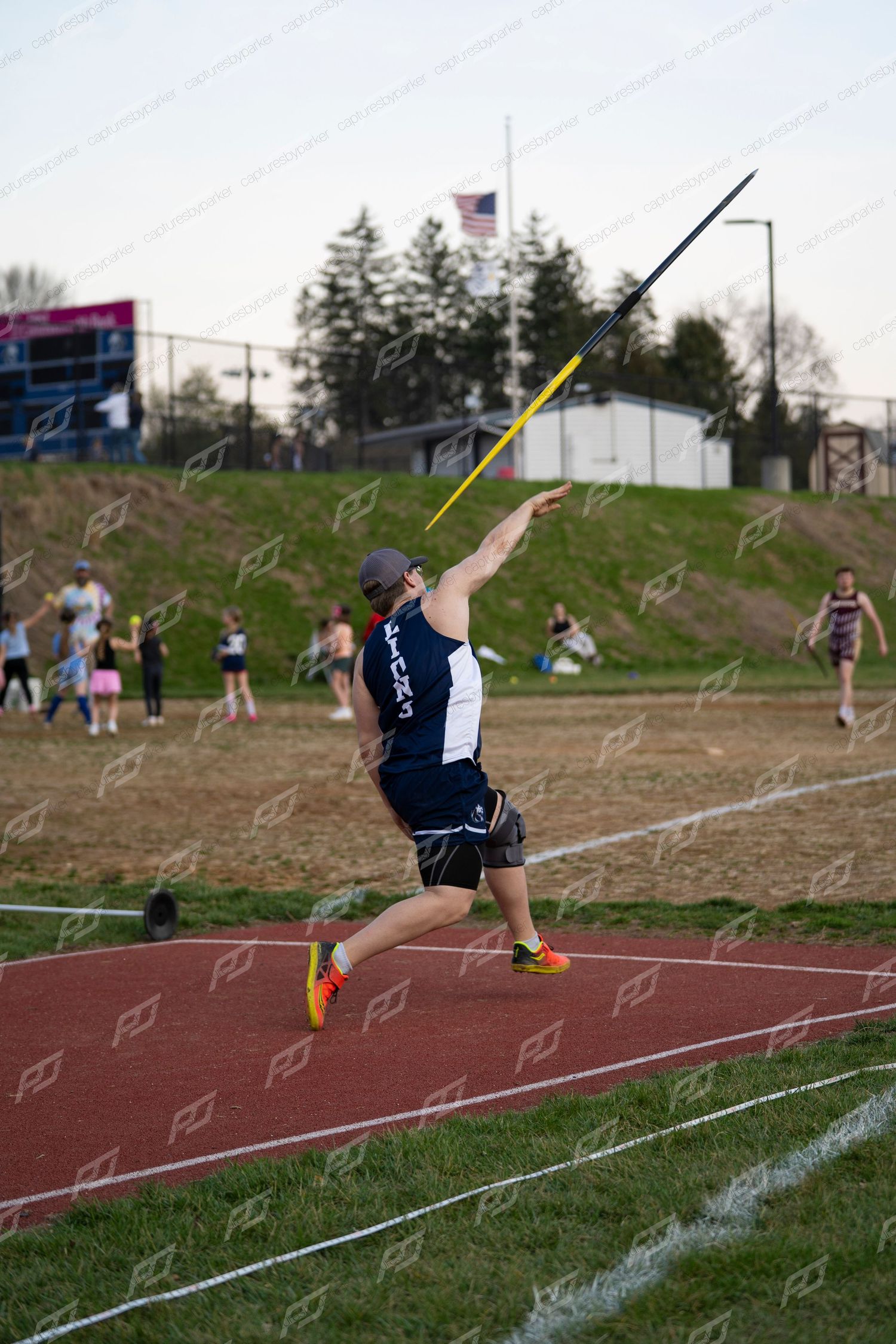 Male athlete in navy Lions uniform throwing javelin at track meet.