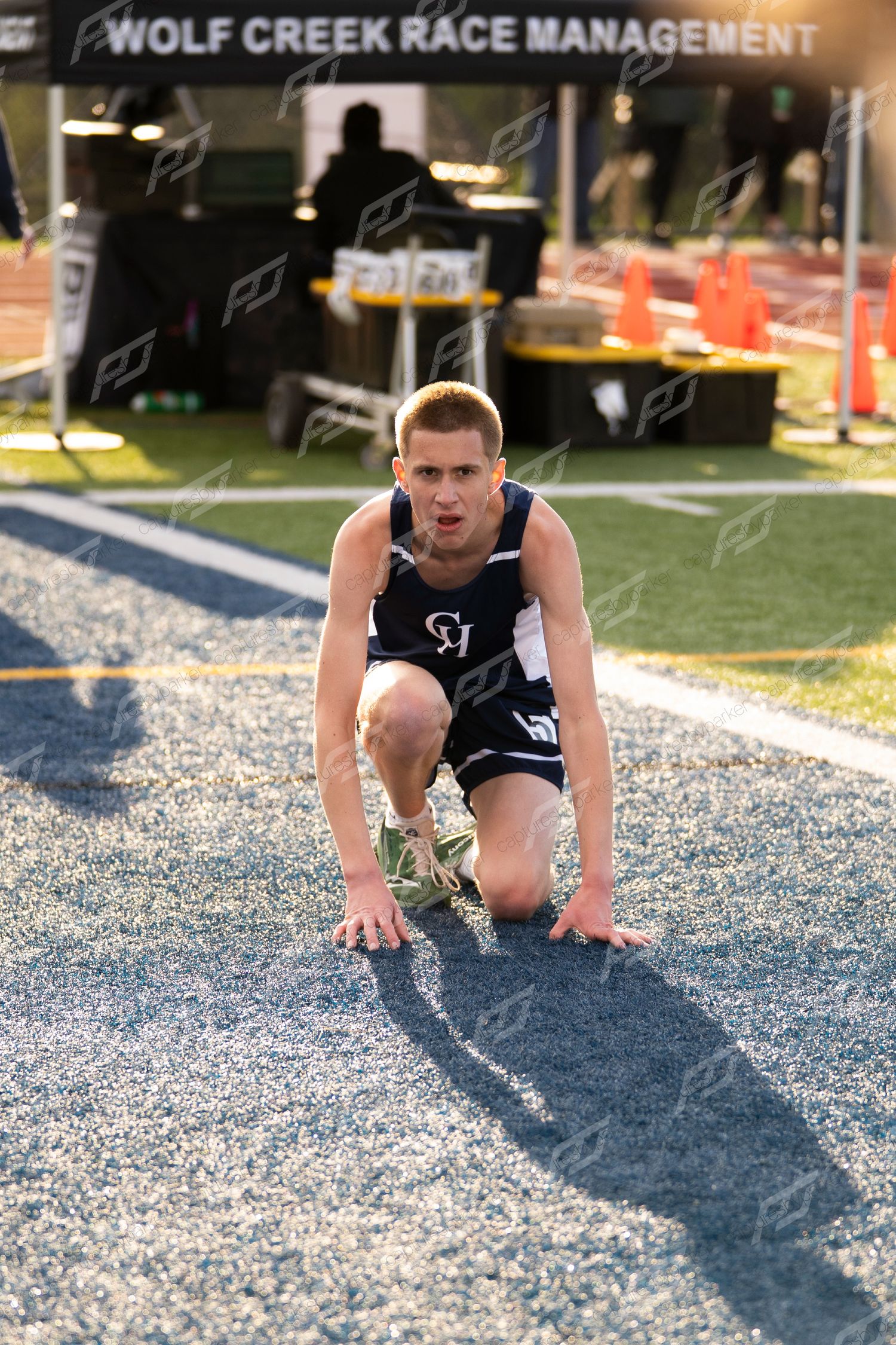 Male high school athlete in navy CH uniform crouches on blue long jump landing pit.