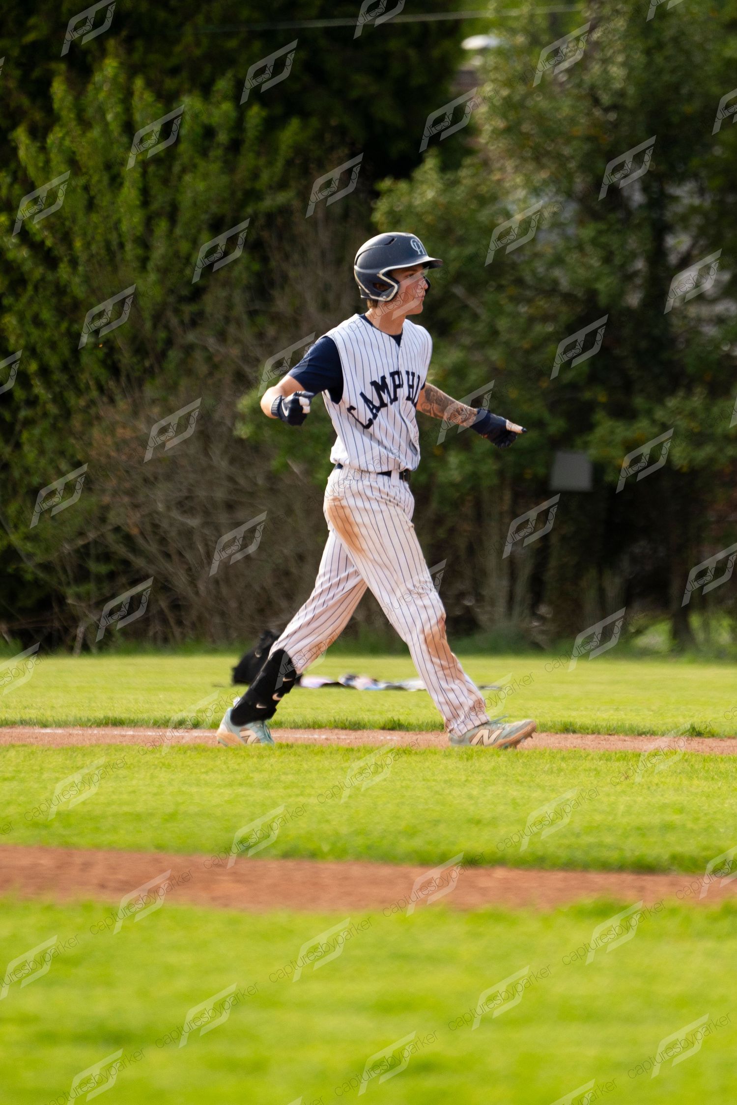 A young baseball player in white pinstripe uniform jogs along the baseline during an outdoor game.