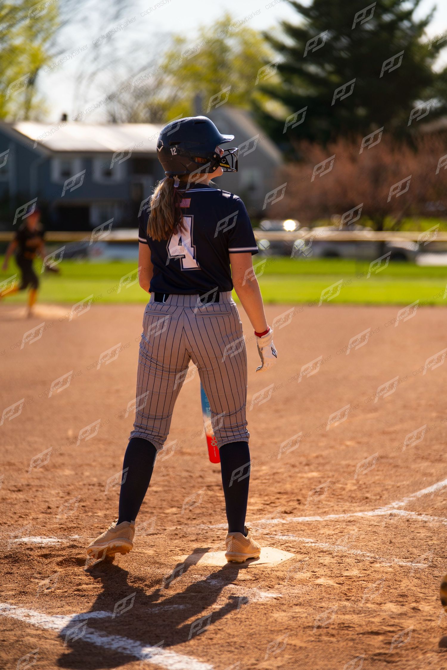 Softball player wearing number 4 navy pinstripe uniform stands at home plate during an outdoor game.