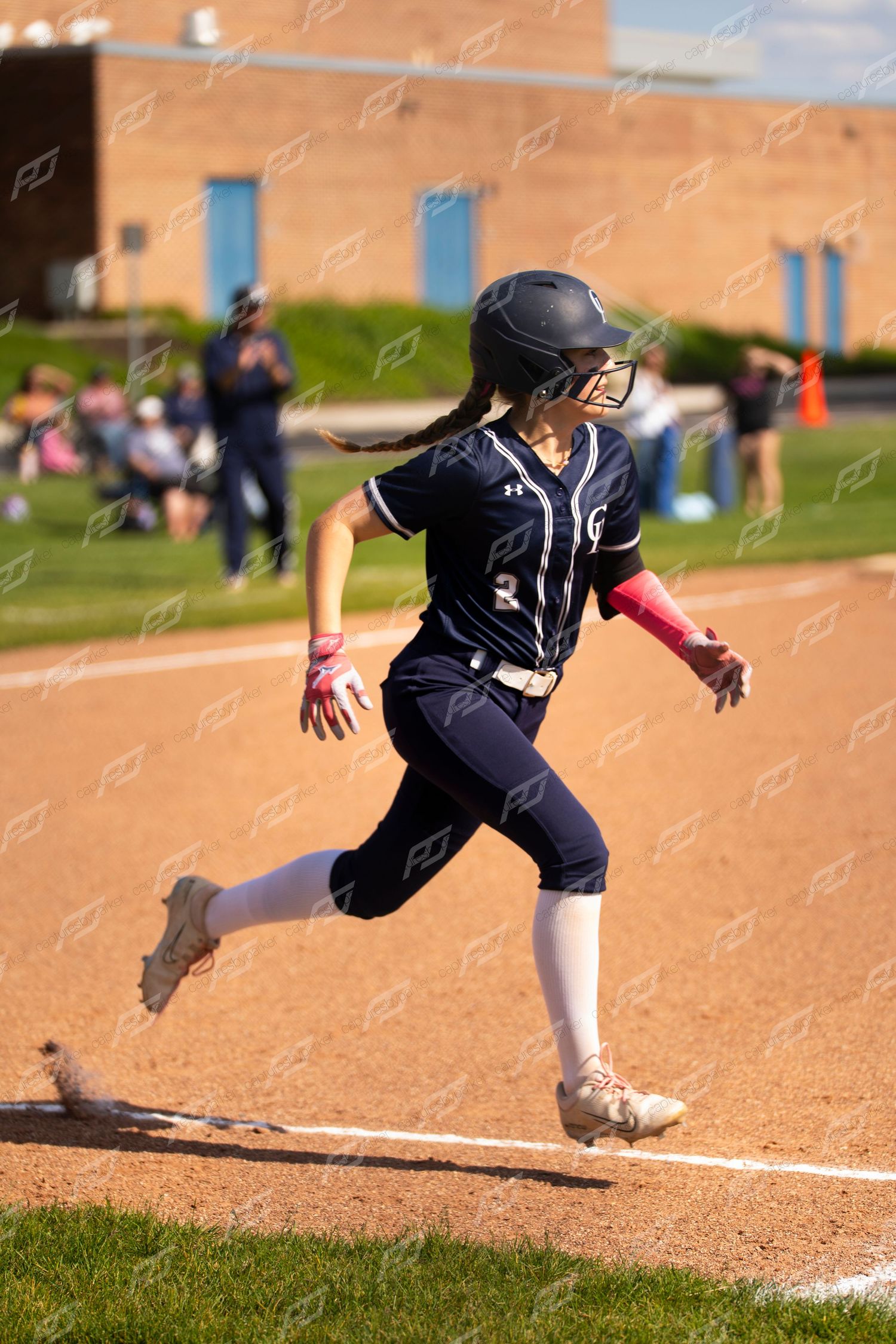 Female softball player in navy uniform runs toward first base after hitting the ball.
