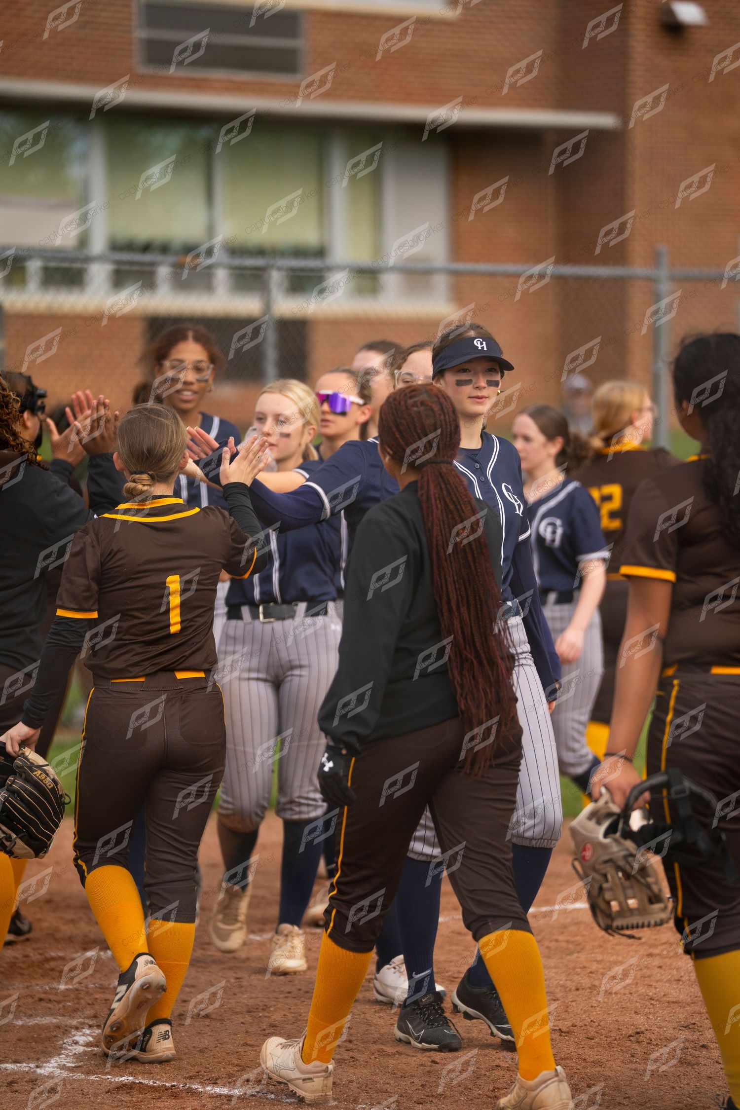 Two softball teams shake hands in a sportsmanlike post-game line on the field.
