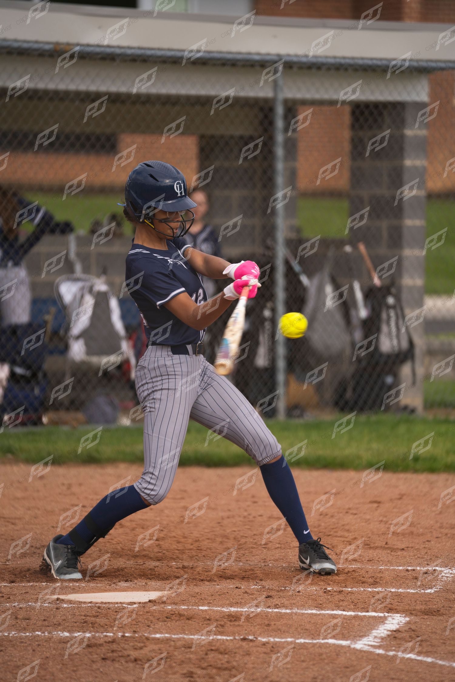 Softball player in navy pinstripe uniform swinging at a yellow ball during a game.