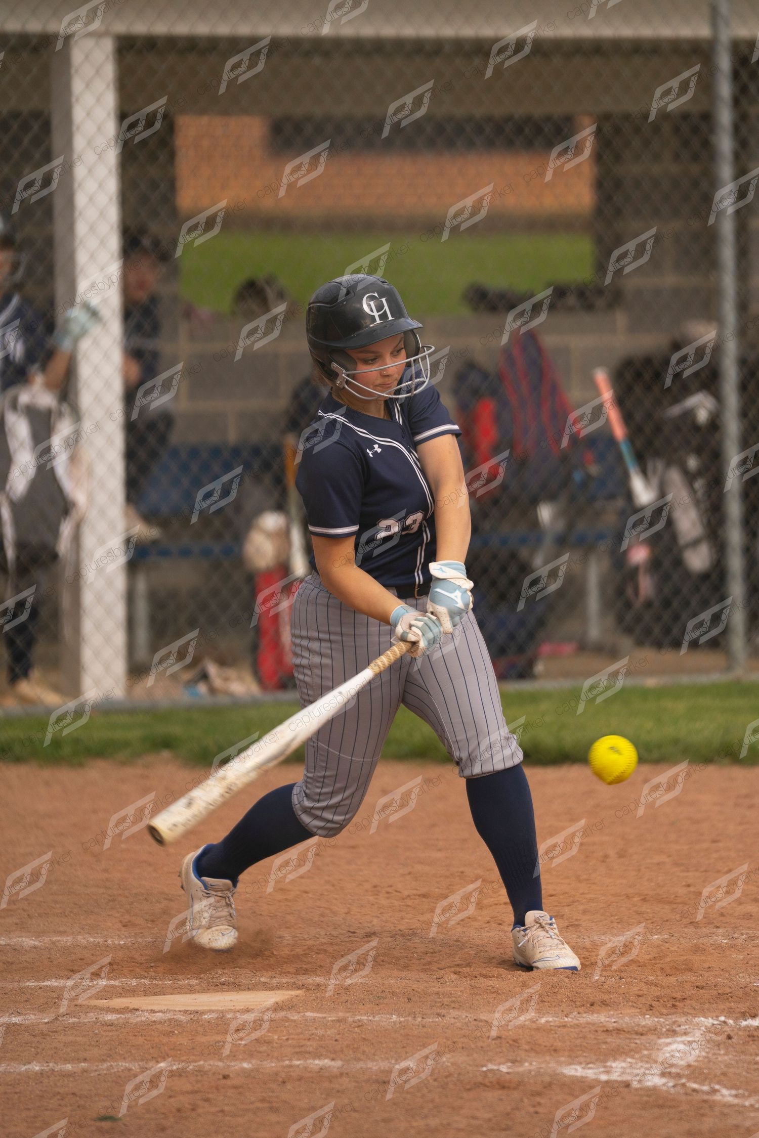 Female softball batter in navy pinstripe uniform making contact with yellow ball.
