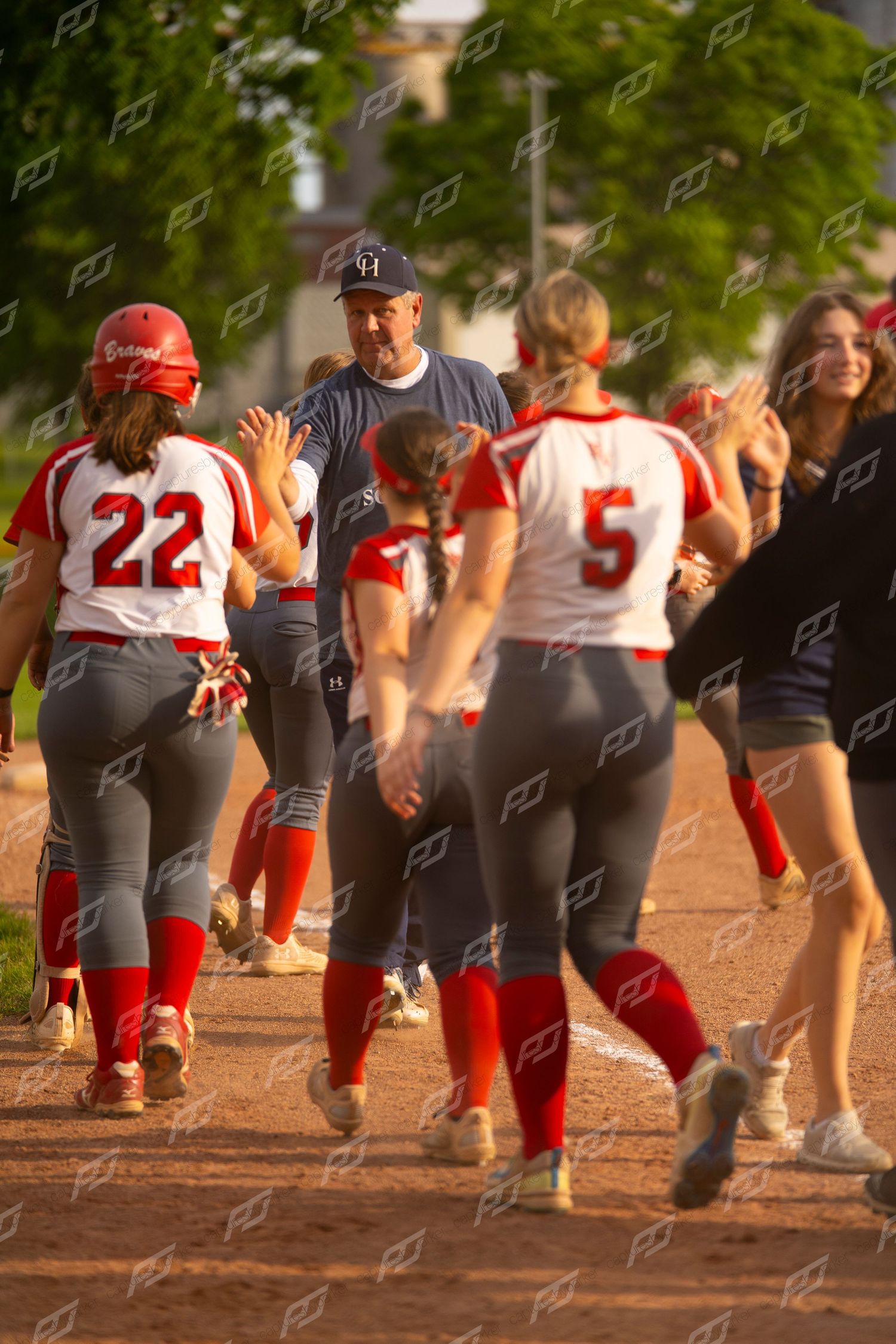 Softball coach in navy congratulates players number 22 and 5 in red uniforms.