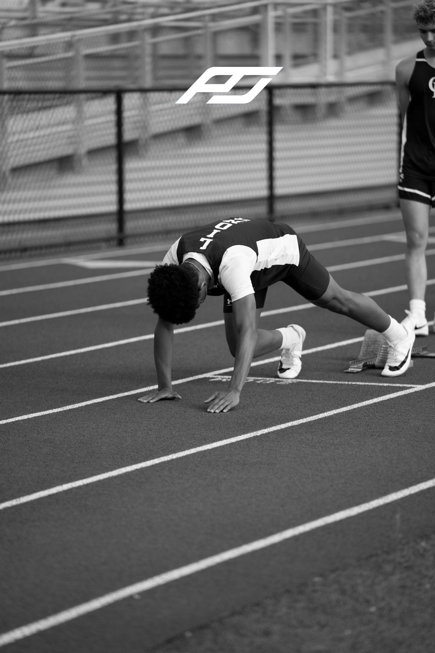 Sprinter in deep starting stance on outdoor track preparing for relay race start.