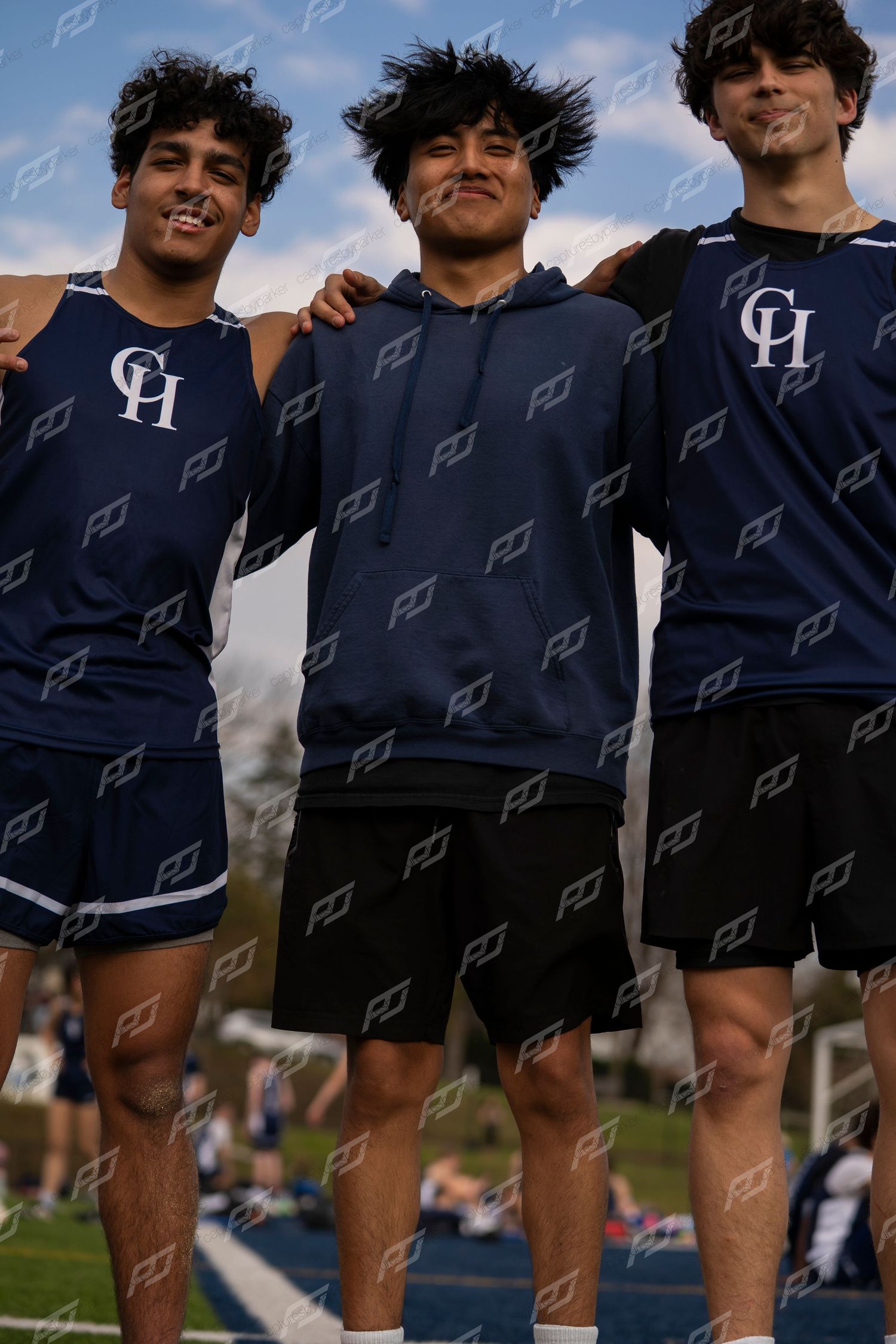 Three male track athletes in navy CH uniforms posing together with arms around shoulders.