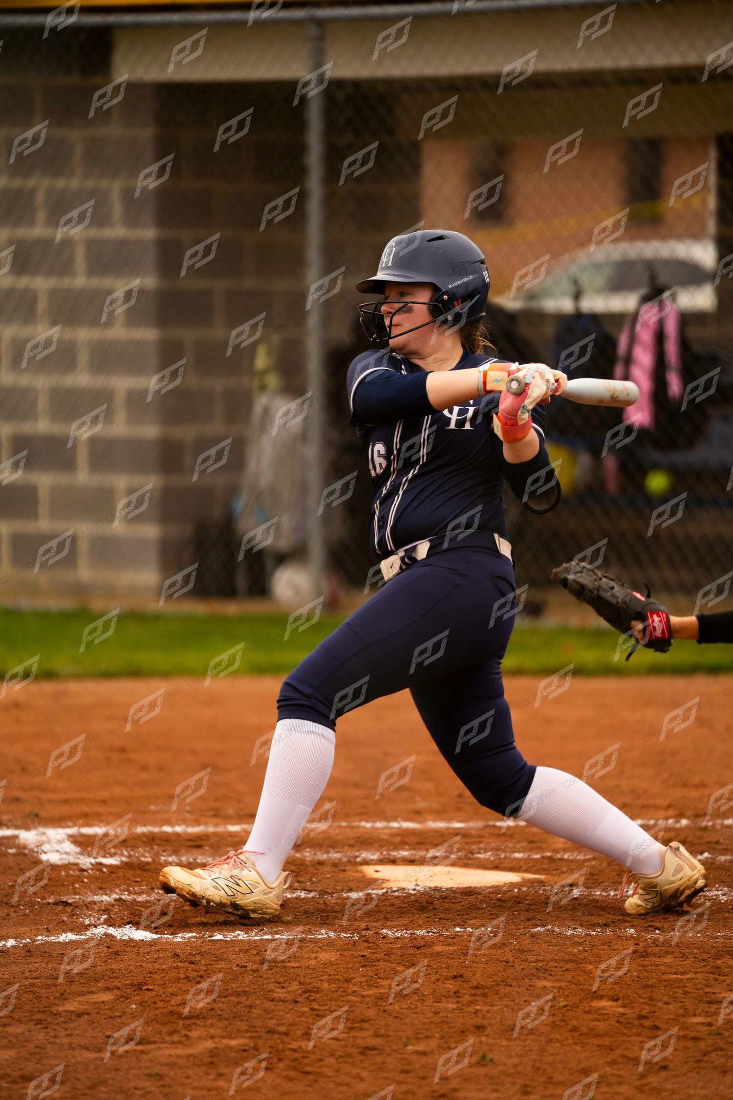 Female softball player in navy uniform completing a powerful swing at home plate during a game.