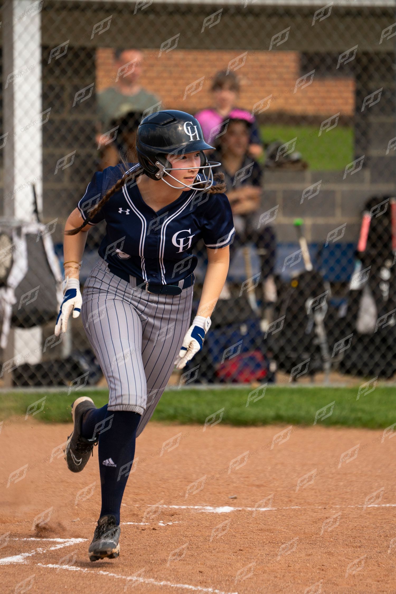 Female softball player in navy pinstripe uniform sprints from home plate after making contact with ball.