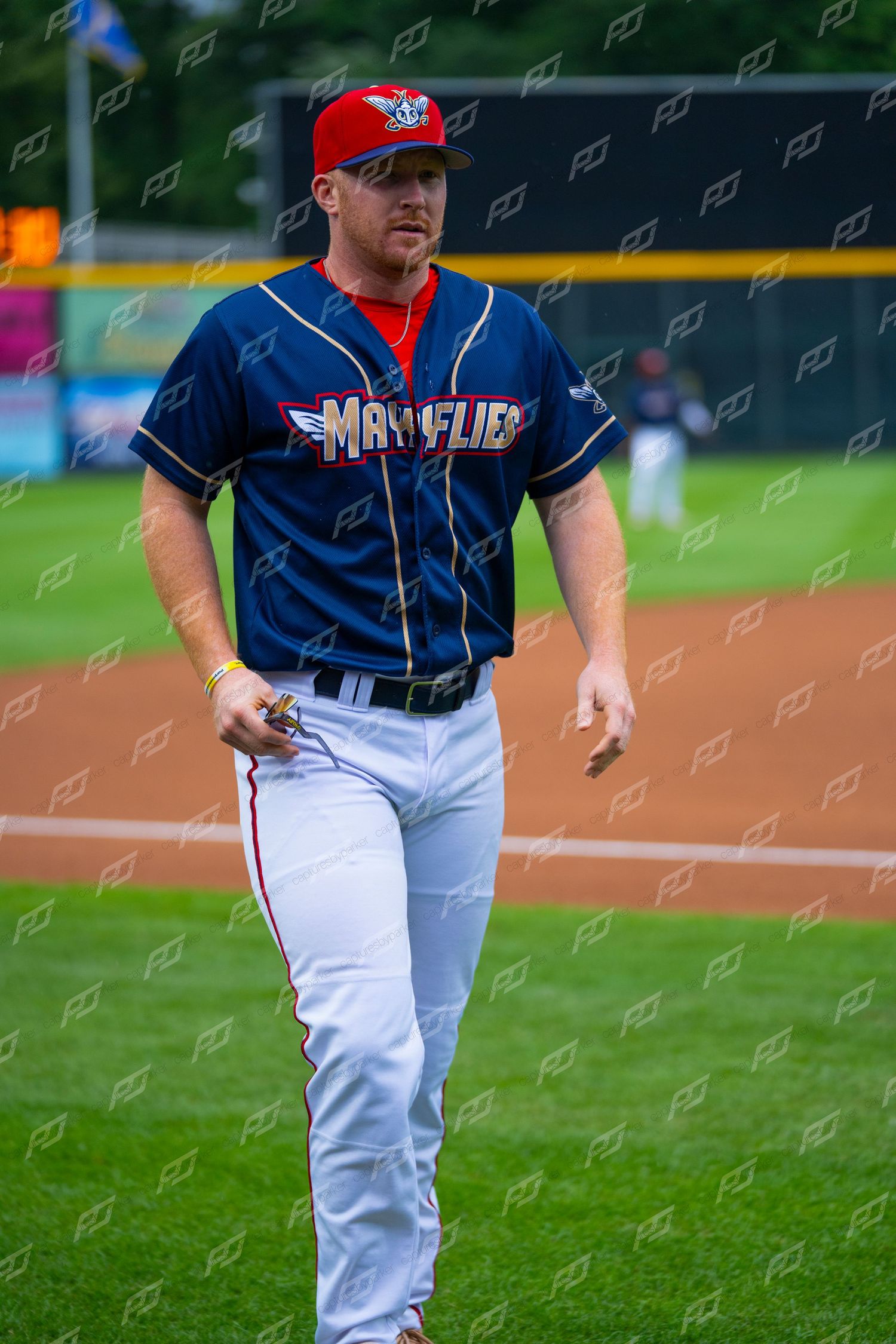 Minor league baseball player in Mayflies navy uniform walking across the field before a game.