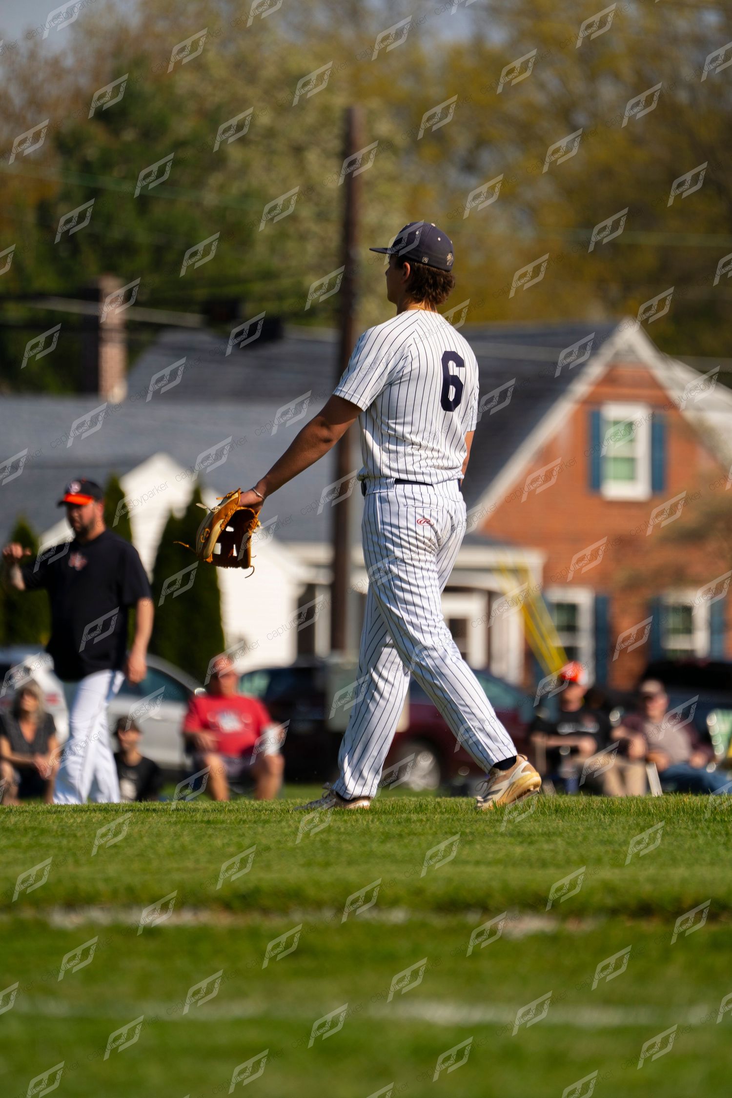 Baseball player #6 in white pinstripe uniform walks on the field with spectators watching in background.