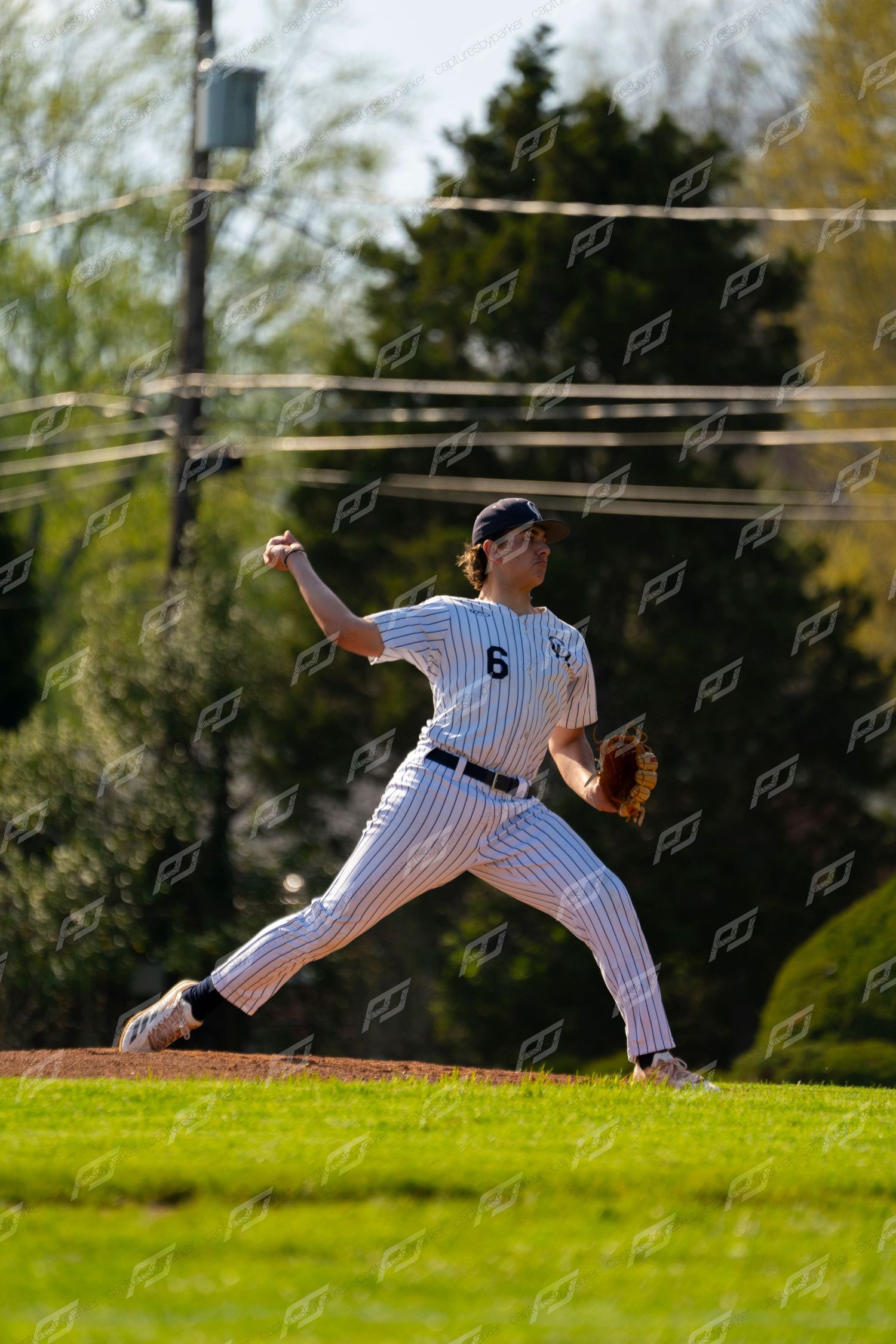 Baseball pitcher #6 in white pinstripe uniform winds up to throw during an outdoor game on a sunny day.