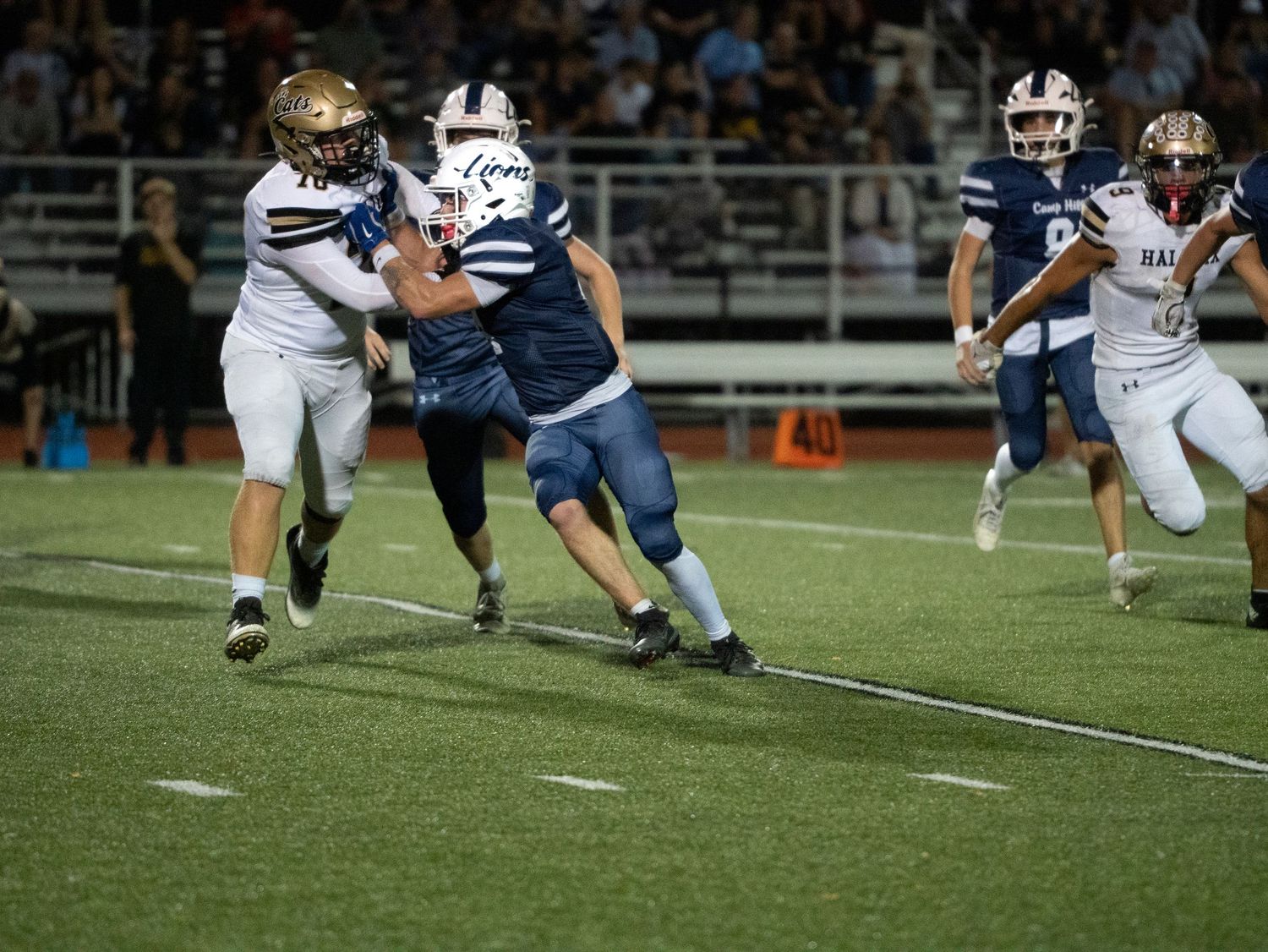 Camp Hill Lions football player tackled by opponent in gold uniform during a night high school game.